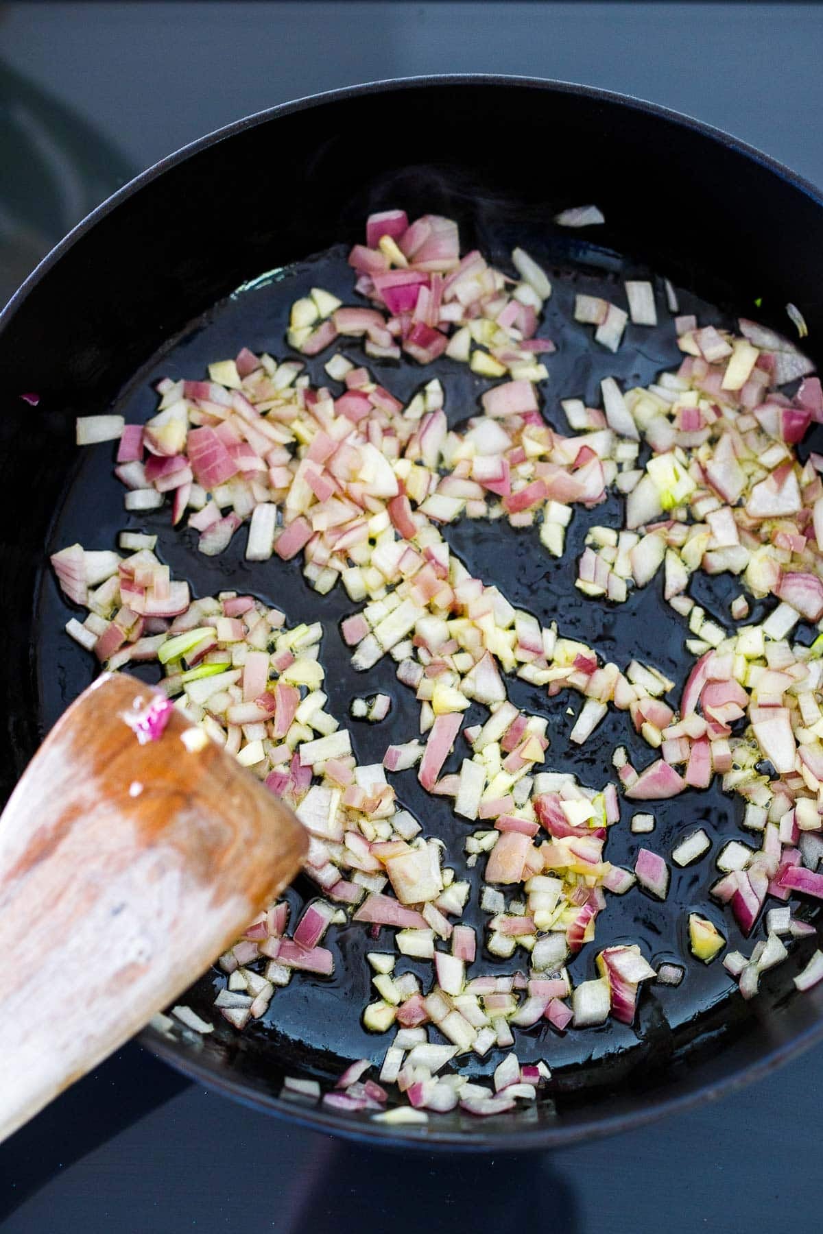 skillet with diced onions and garlic with wood spatula.