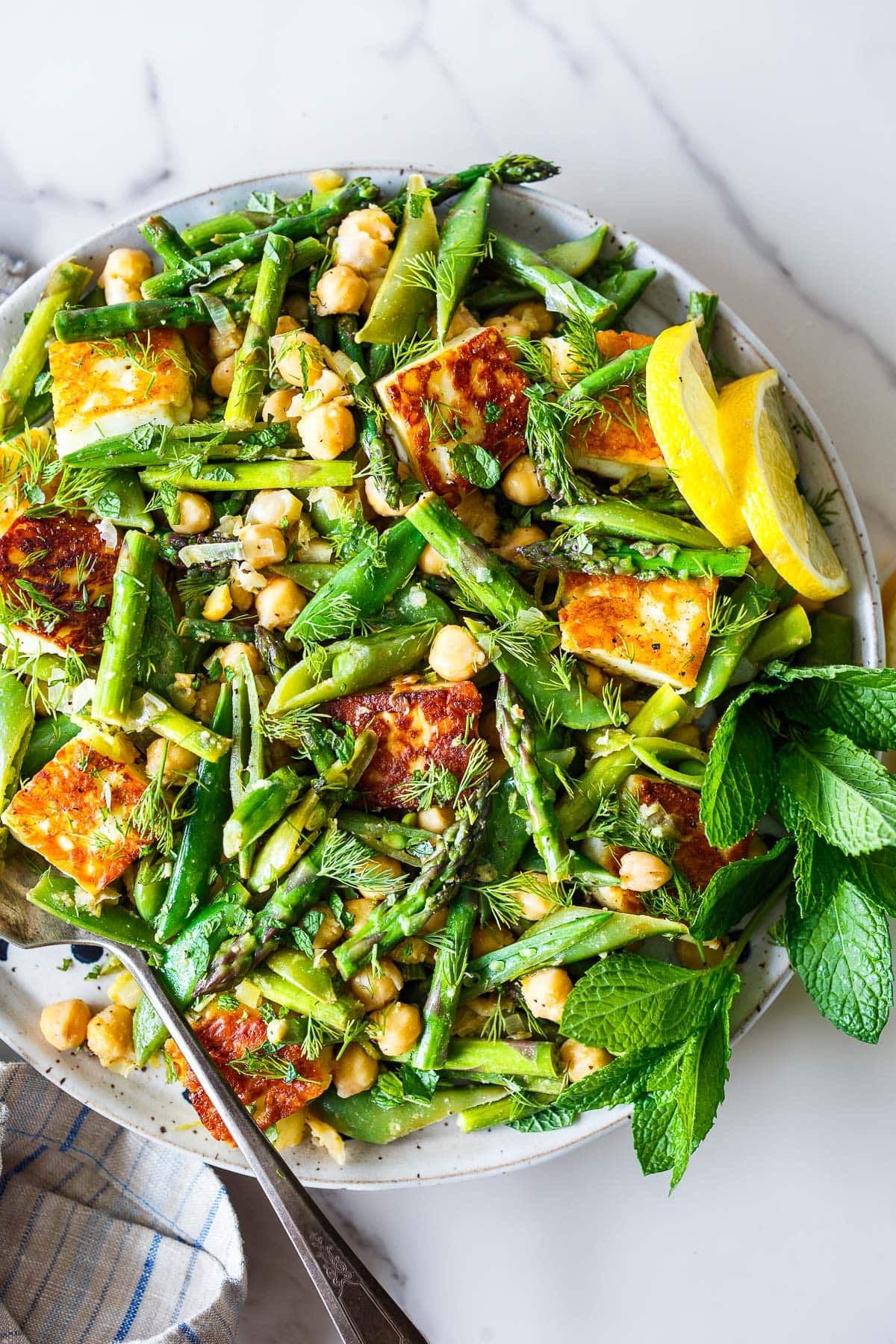 serving dish with halloumi recipe with asparagus, snap peas, dill, mint, chickpeas, lemon slices, and seared halloumi.