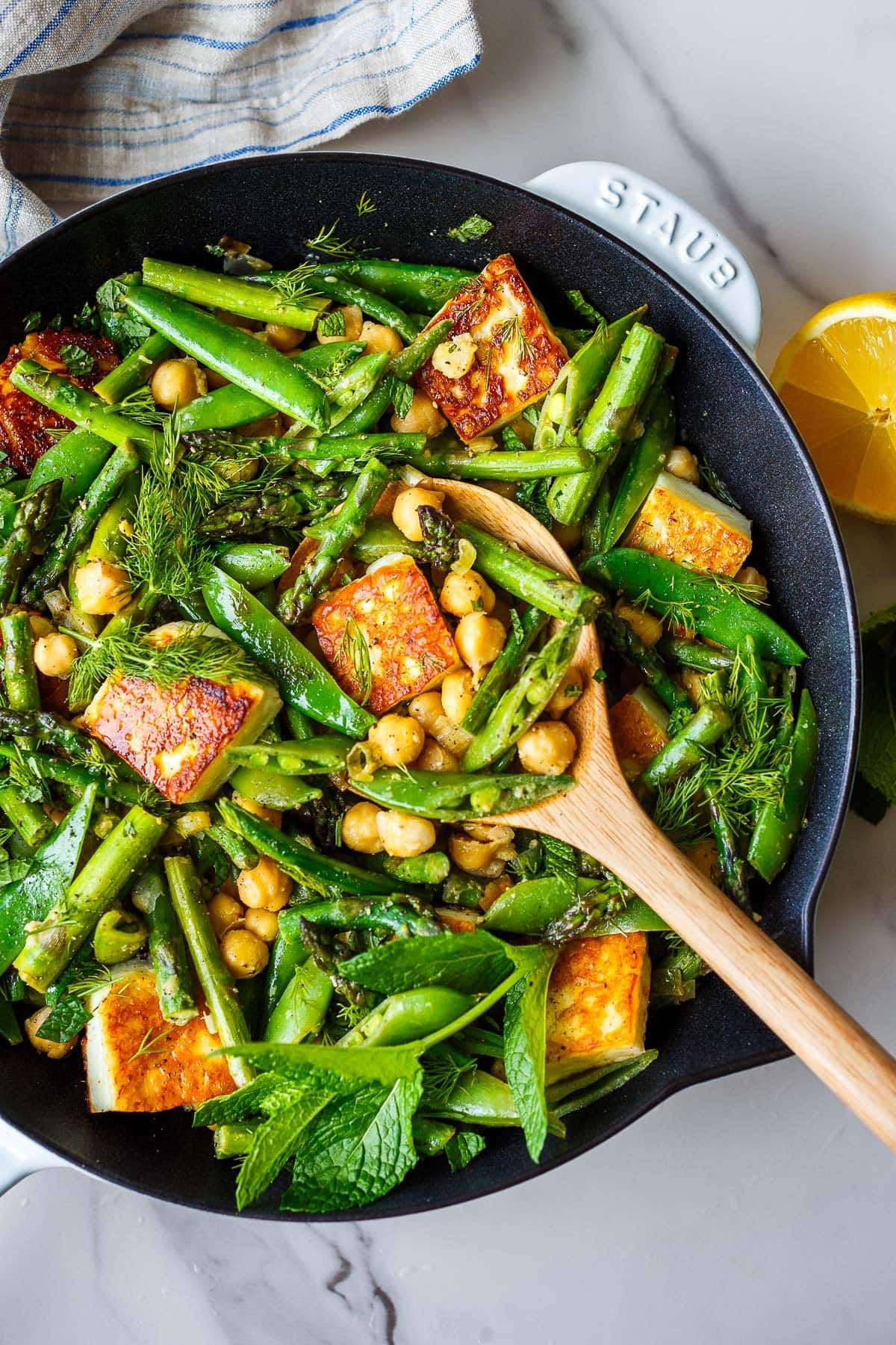 one-pan seared halloumi recipe with snap peas, asparagus, chickpeas, dill, mint, with wooden serving spoon.
