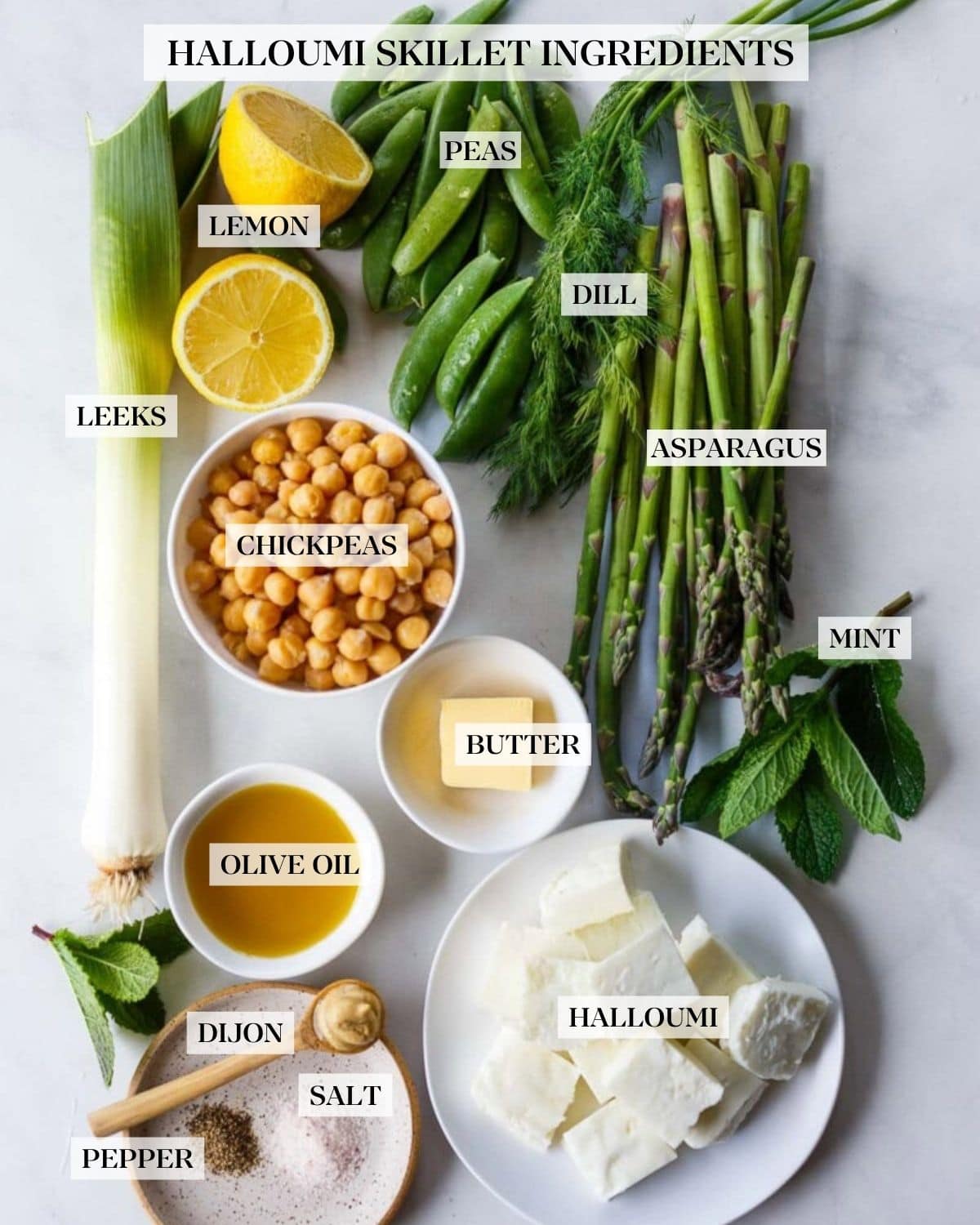 ingredients for a halloumi recipe - snap peas, dill, asparagus, mint, lemon halves, leek, bowl of chickpeas, pat of butter, small bowl of olive oil, small dish with salt and pepper with a wood spoon of Dijon mustard, and small plate of halloumi squares.