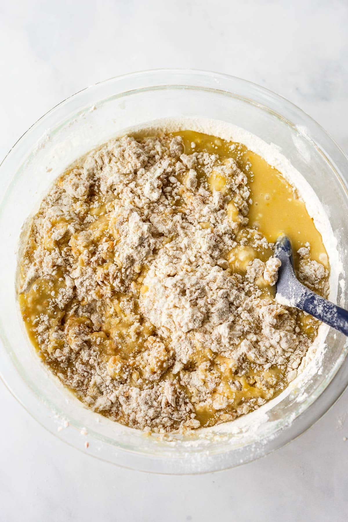 glass mixing bowl with batter for lemon bundt cake with spatula folding flour in.