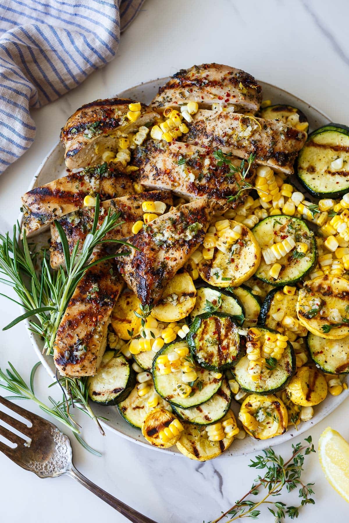 platter of Mediterranean grilled chicken, grilled corn, and grilled zucchini and fresh rosemary.