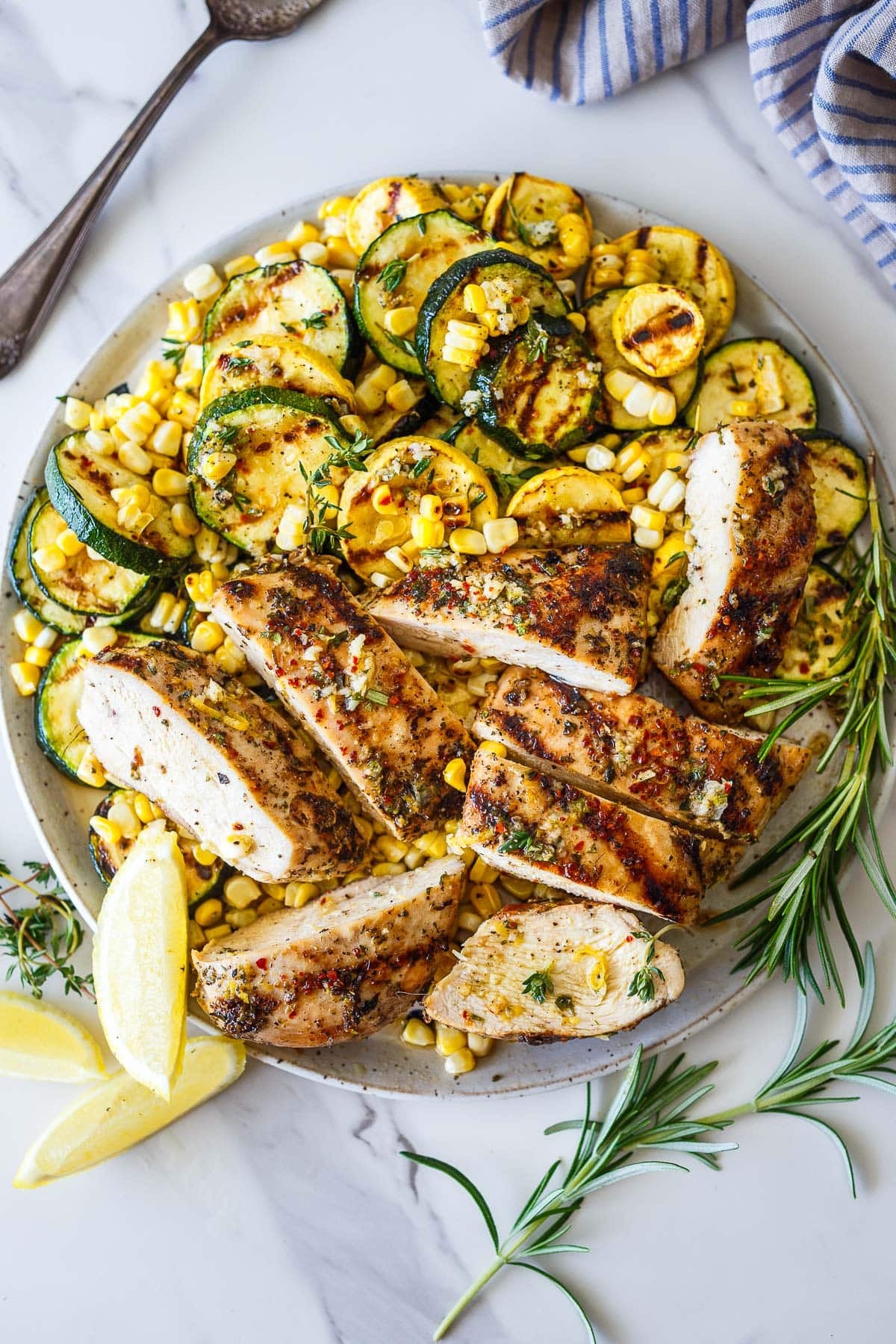 plate of Mediterranean grilled chicken, grilled zucchini, and grilled corn, with a sprig of rosemary.