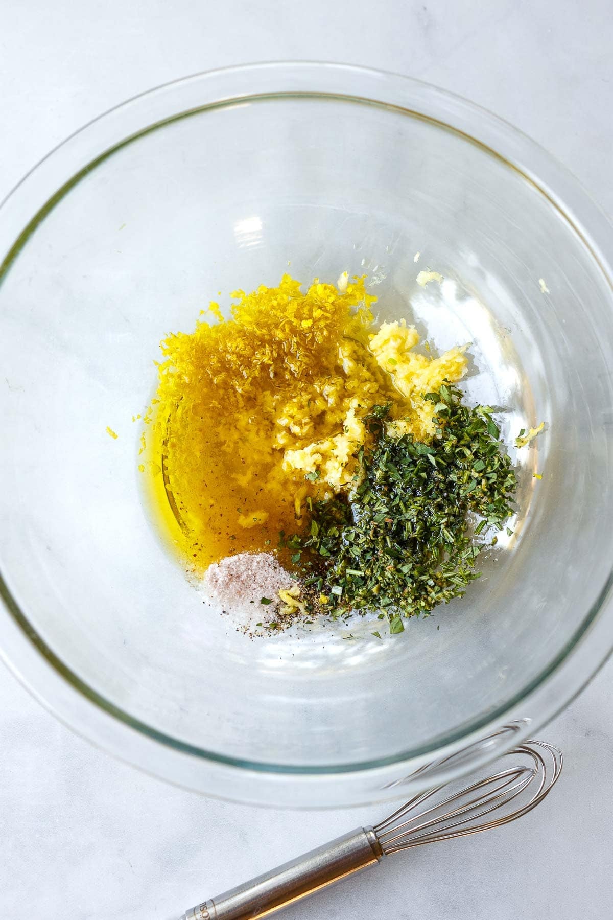 glass mixing bowl with lemon herb marinade for Mediterranean grilled chicken.