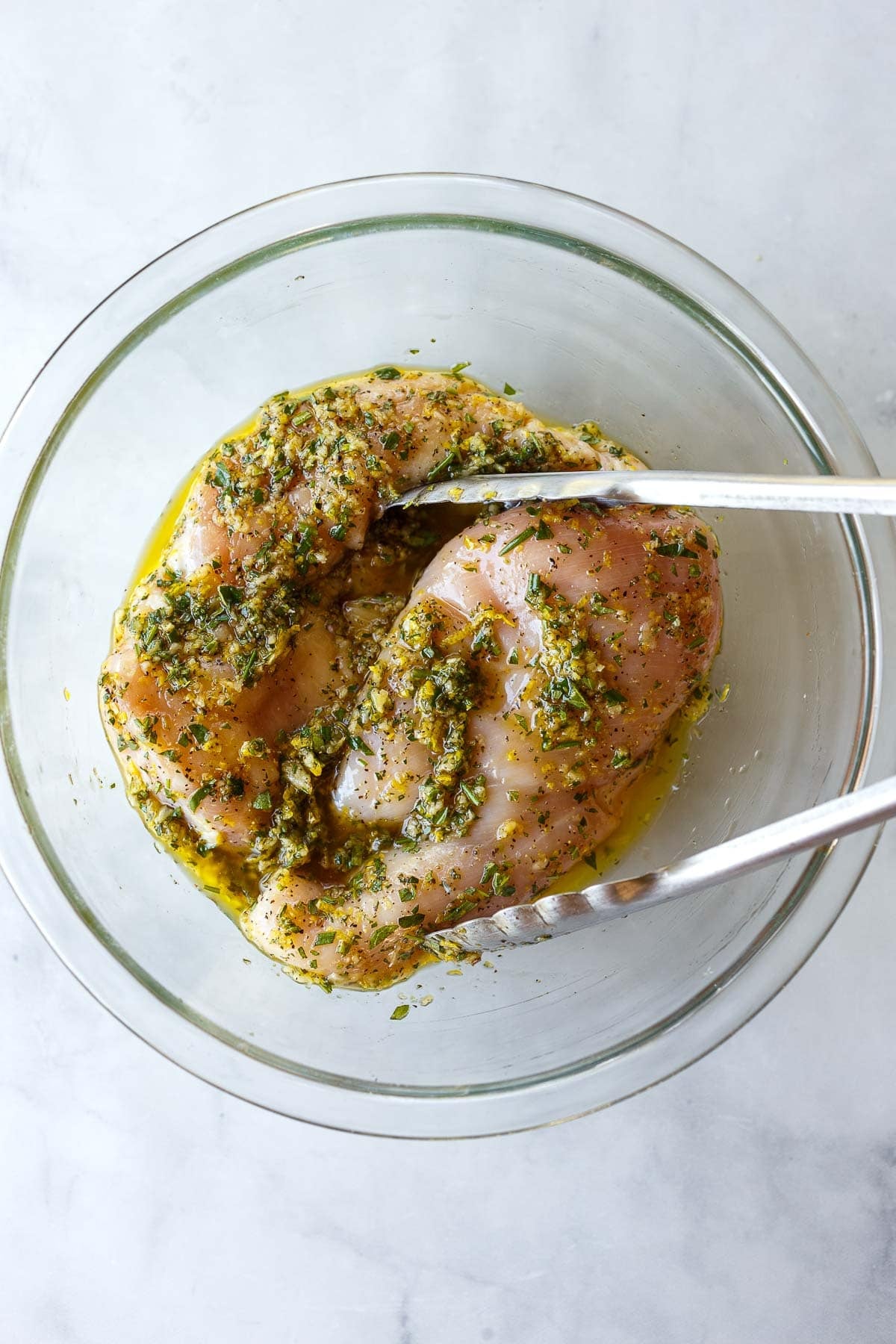 tongs tossing the chicken in the marinade in a glass bowl.