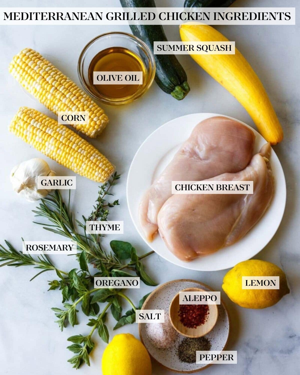 ingredients for Mediterranean grilled chicken - zucchini and yellow squash, ears of corn, bowl of oil, plate of chicken breasts, garlic bulb, fresh herbs, lemons, and small dish of salt, pepper, and chili flakes.