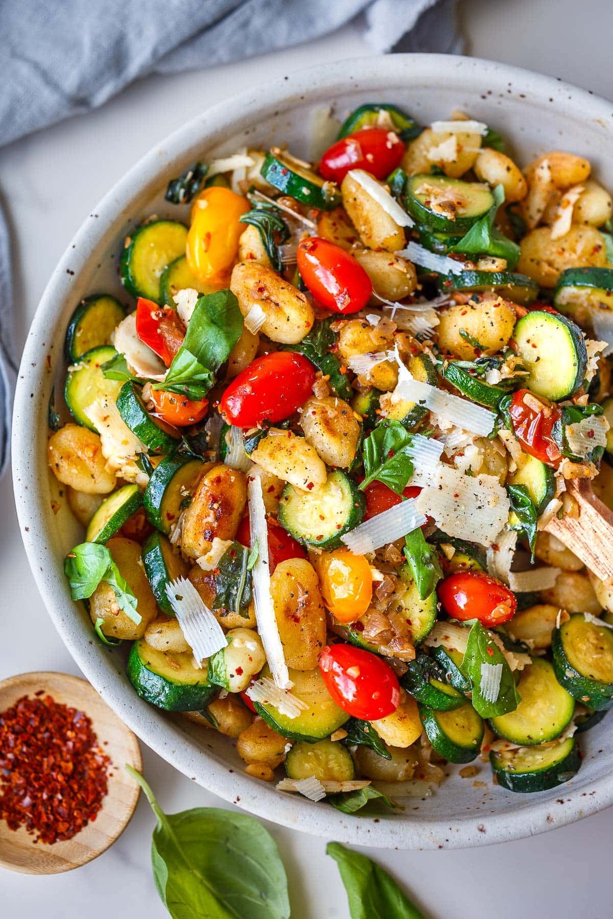 bowl of pan-fried gnocchi with zucchini slices and cherry tomatoes, red pepper flakes, basil, and grated pecorino.