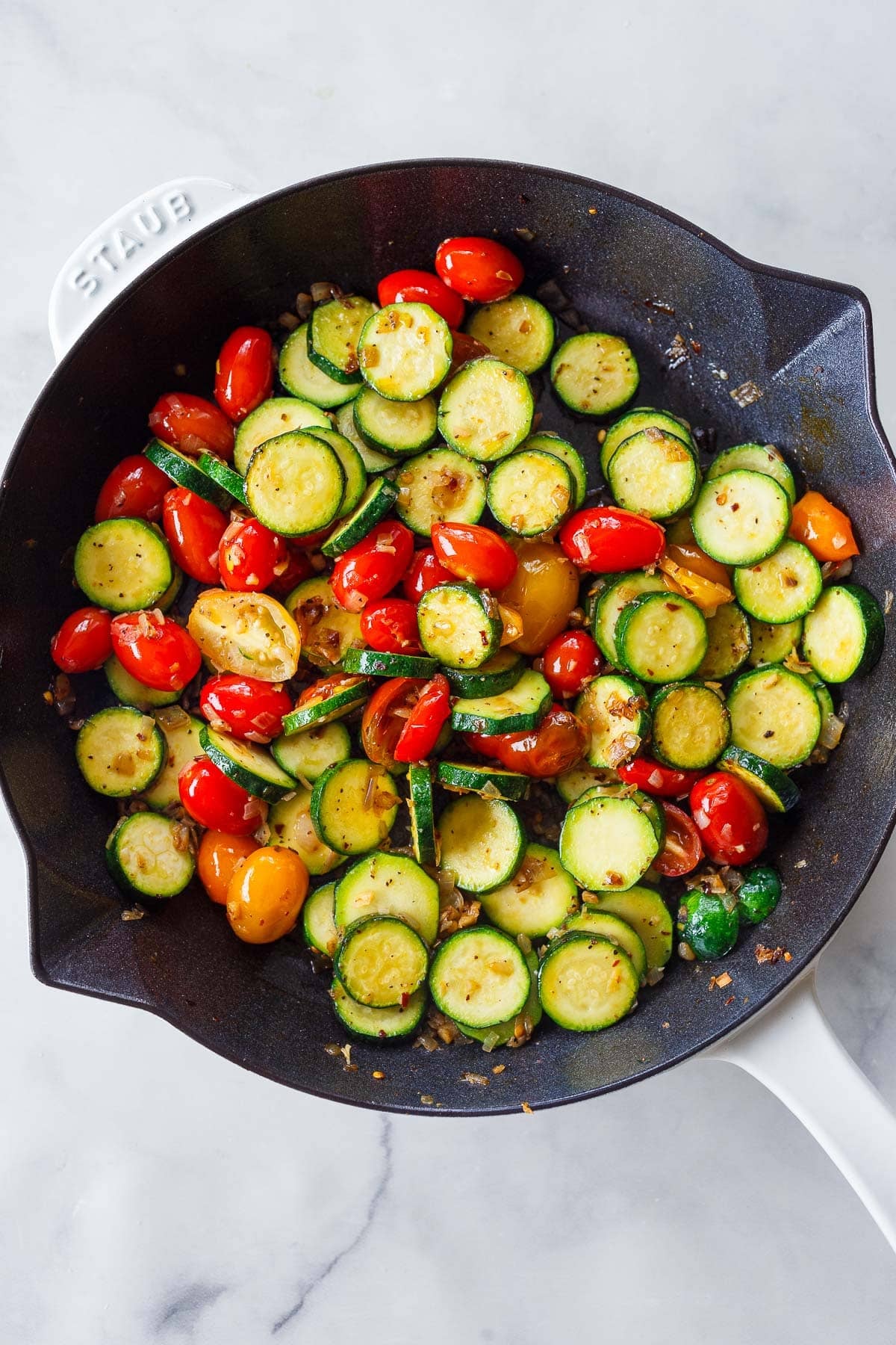 zucchini slices and cherry tomatoes sautéing in a skillet.