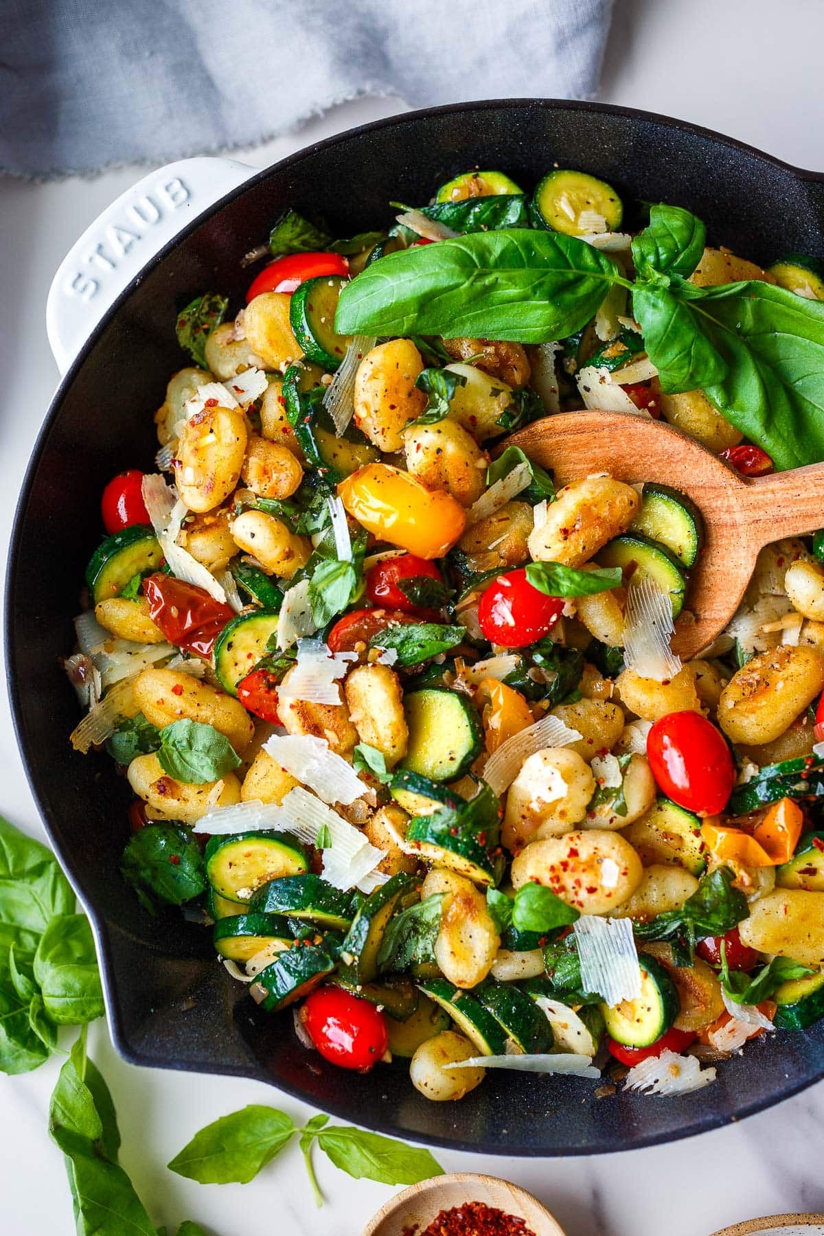 pan-fried gnocchi with sautéed zucchini and cherry tomatoes with red pepper flakes, basil, and grated pecorino in a skillet with a wooden spoon.