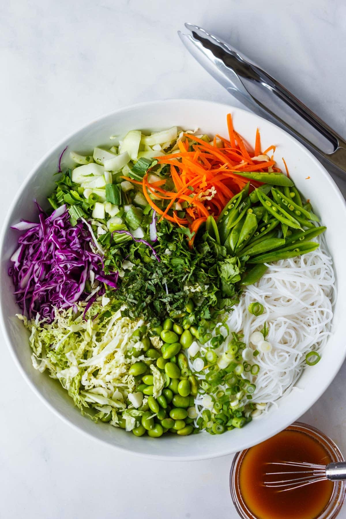 ingredients for Asian noodle salad in a bowl - noodles, herbs, edamame, shredded cabbage, bok choy, carrots, snap peas.