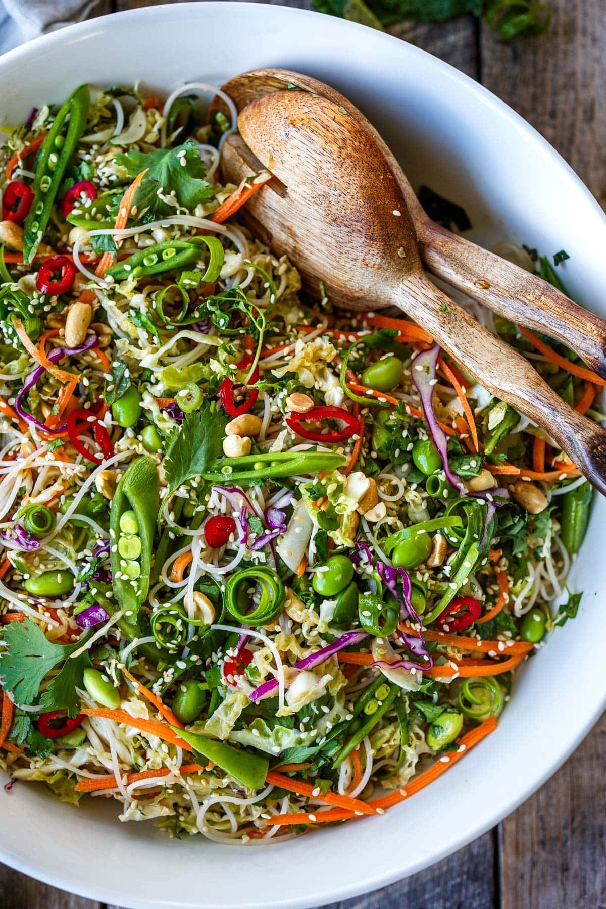 Asian noodle salad in a bowl with shredded carrots and cabbage, herbs, snap peas, peanuts, and sesame seeds.