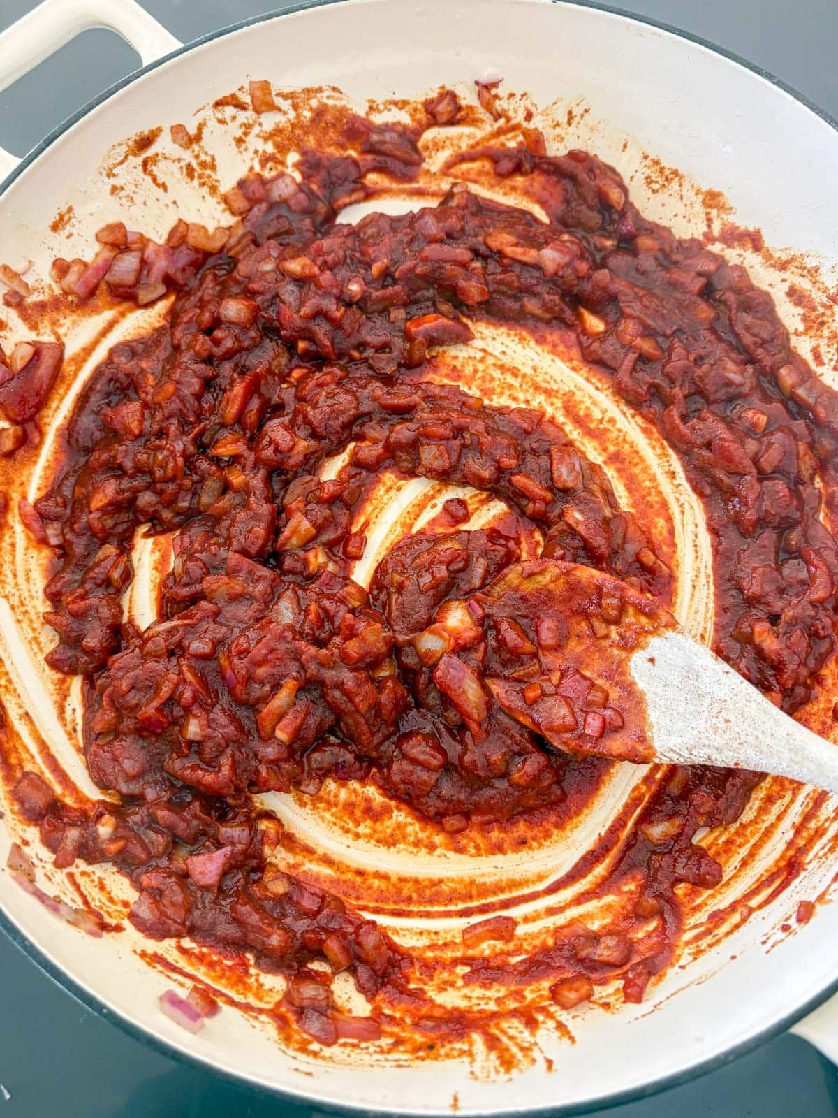 stirring sautéed aromatics with tomato paste in a braiser to make baked beans.