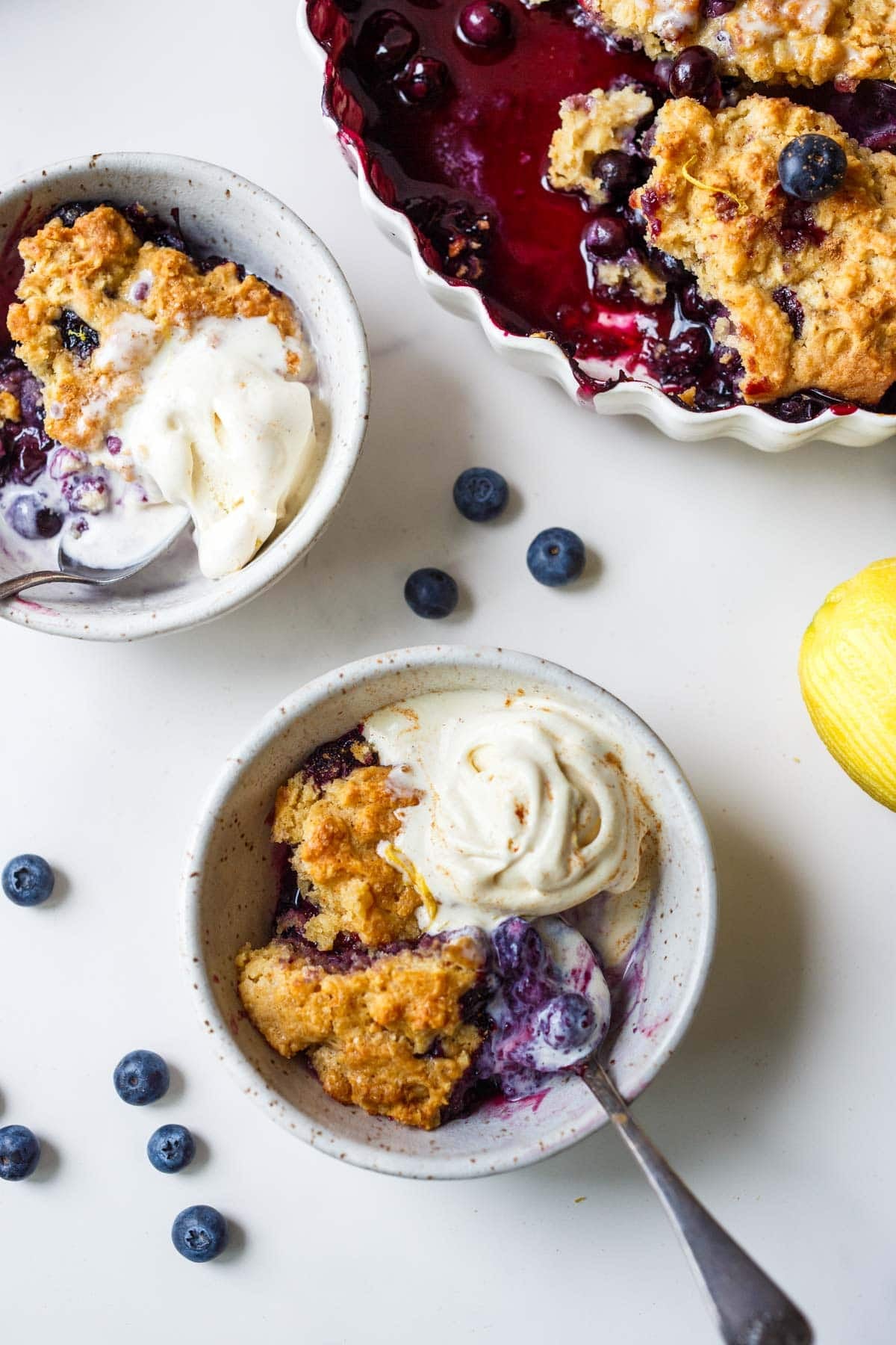 two bowls of blueberry cobbler with ice cream and spoons.