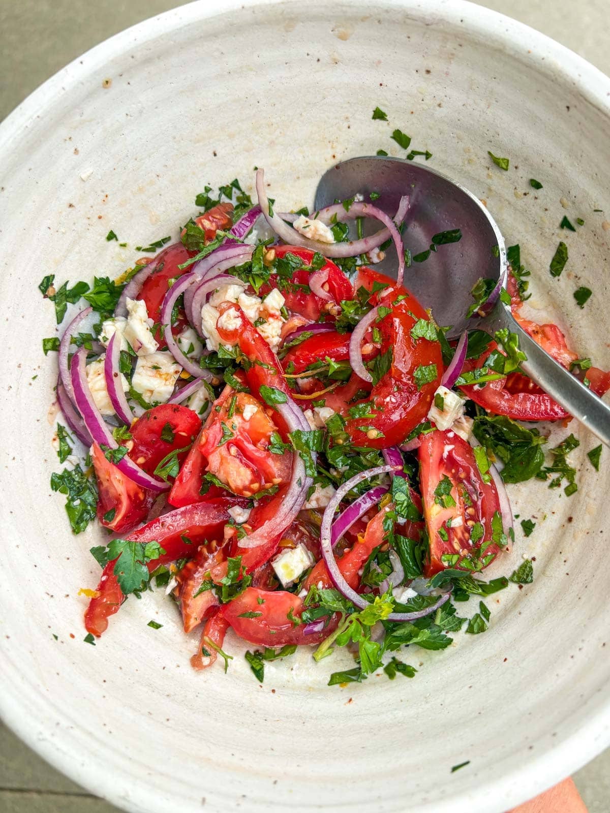 tomato feta salad in bowl with parsley and red onion, with a spoon.