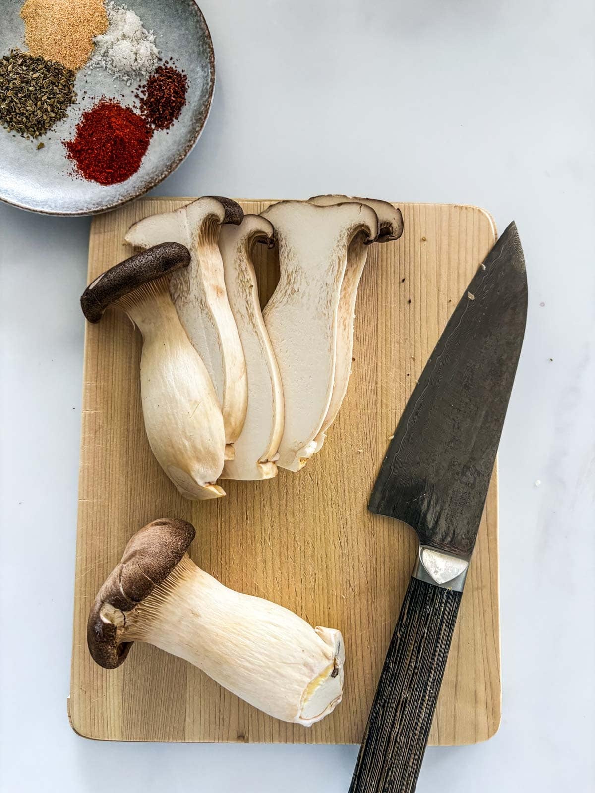 wood cutting board with sliced king oyster mushroom with sharp knife.