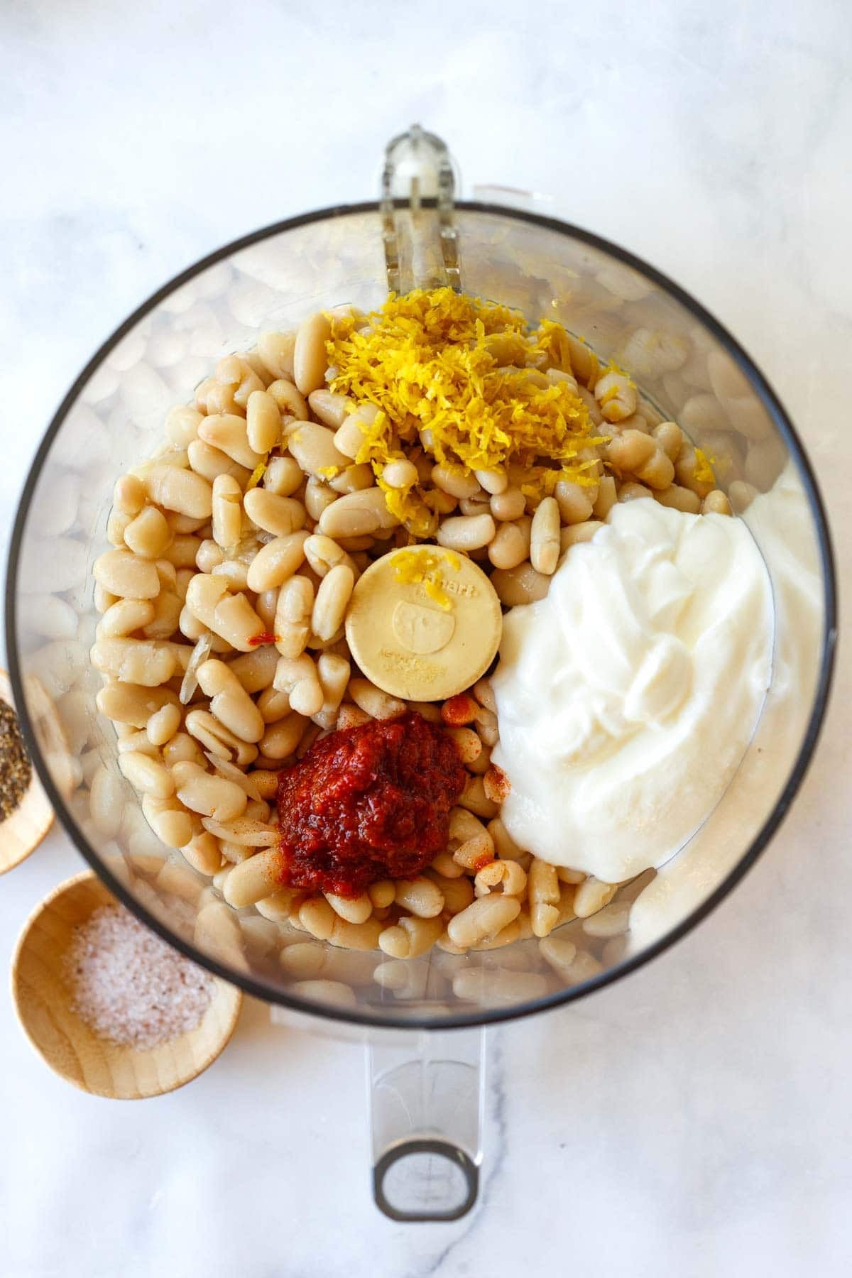 ingredients for harissa white bean puree in food processor - white beans, lemon zest, greek yogurt, and harissa.