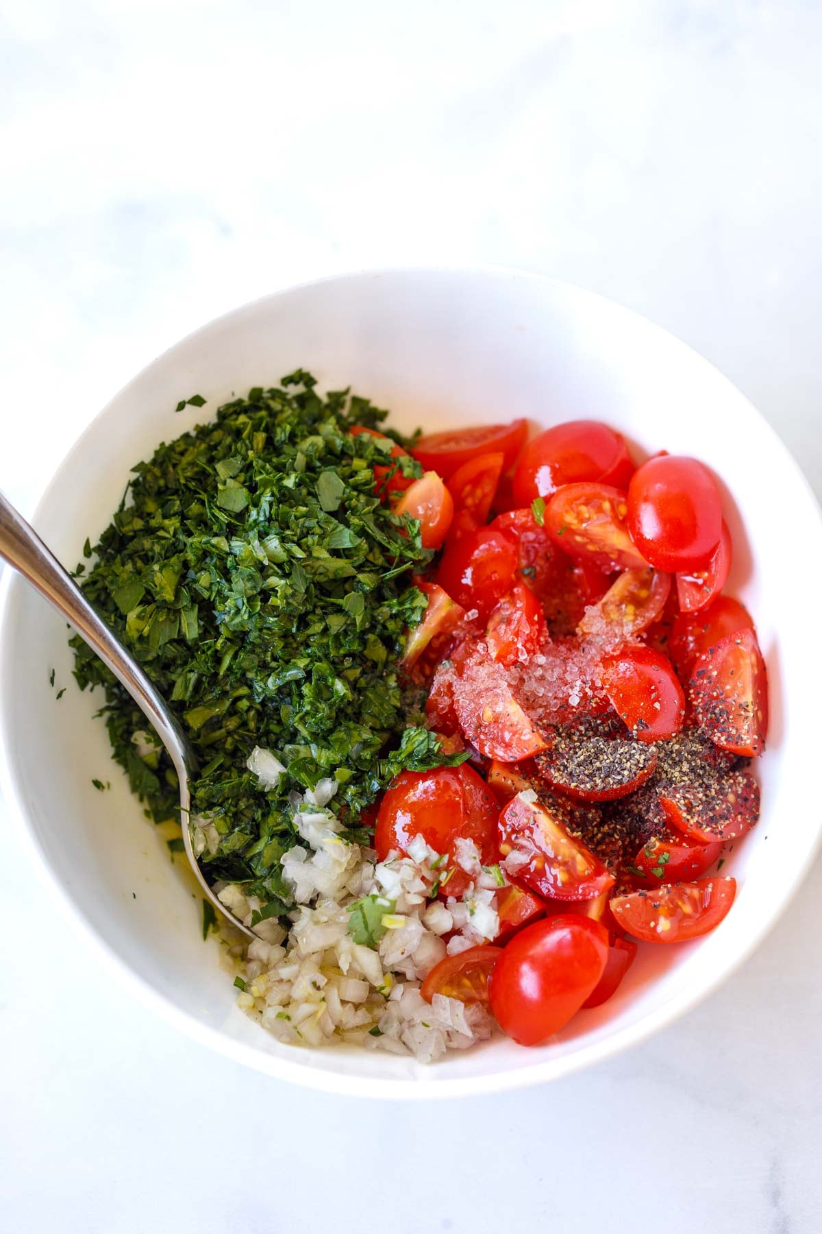 bowl with quartered cherry tomatoes, minced herbs, and minced shallots, with oil, salt, and pepper to make tomato gremolata.