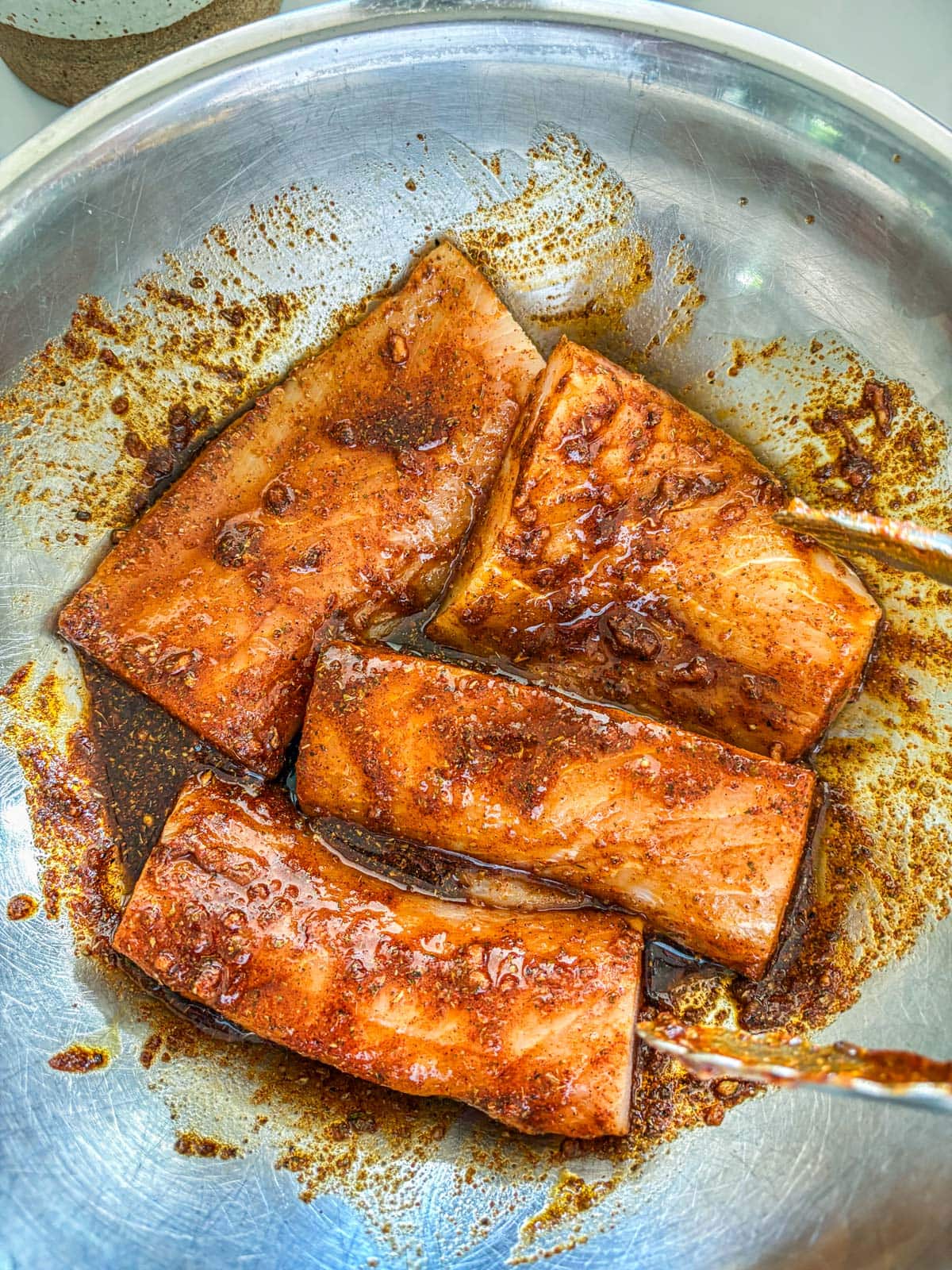 mahi mahi fillets in marinade in a mixing bowl with tongs.