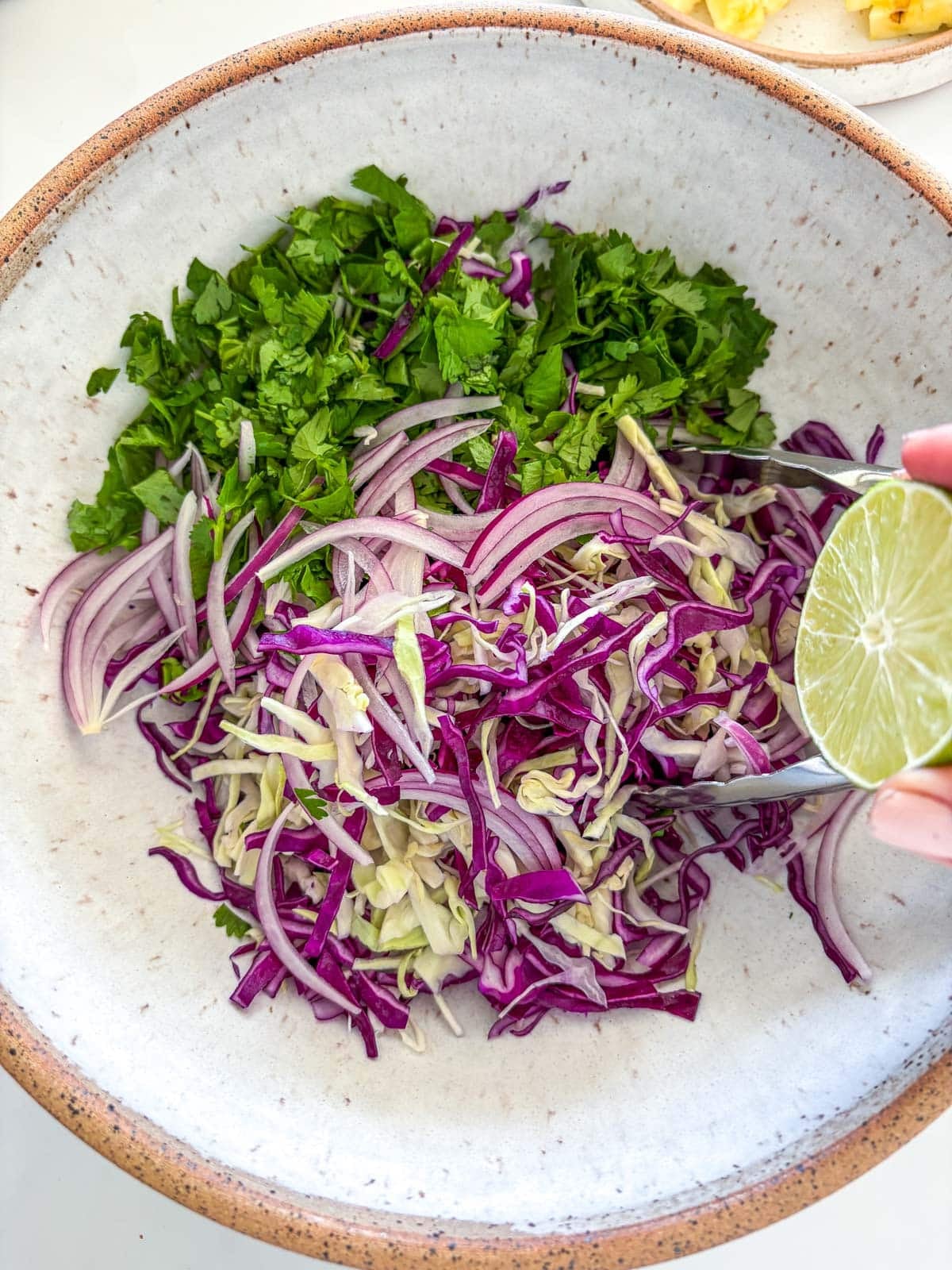 squeezing lime into bowl of shredded cabbage, sliced red onion, and fresh cilantro. 