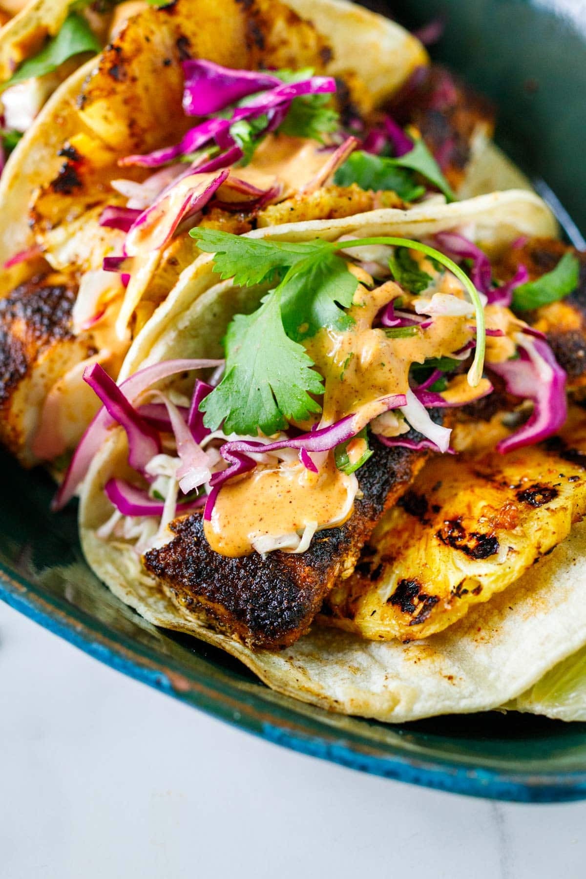 close up of mahi mahi tacos with grilled mahi mahi and pineapple, slaw, cilantro, and chipotle mayo.