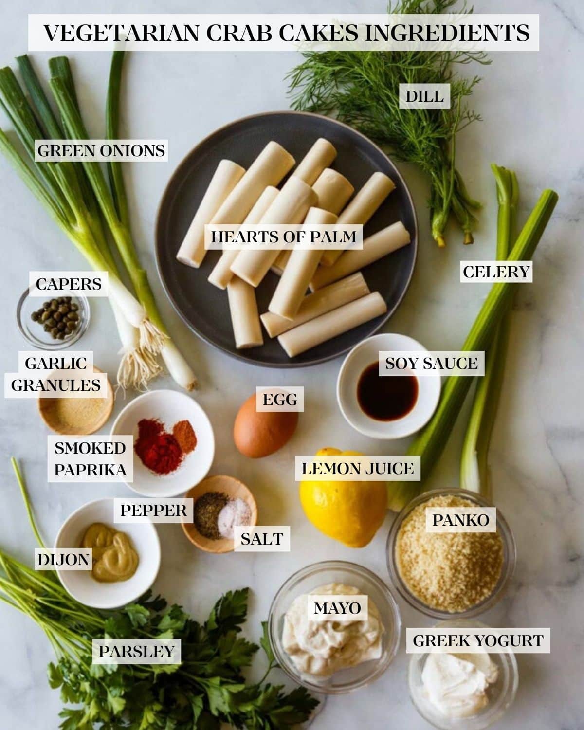 vegetarian crab cakes ingredients arranged and labeled - dill, hearts of palm, green onions, celery, capers, garlic granules, smoked paprika, egg, soy sauce, lemon juice, pepper, salt, Dijon, panko, mayo, parsley, Greek yogurt.