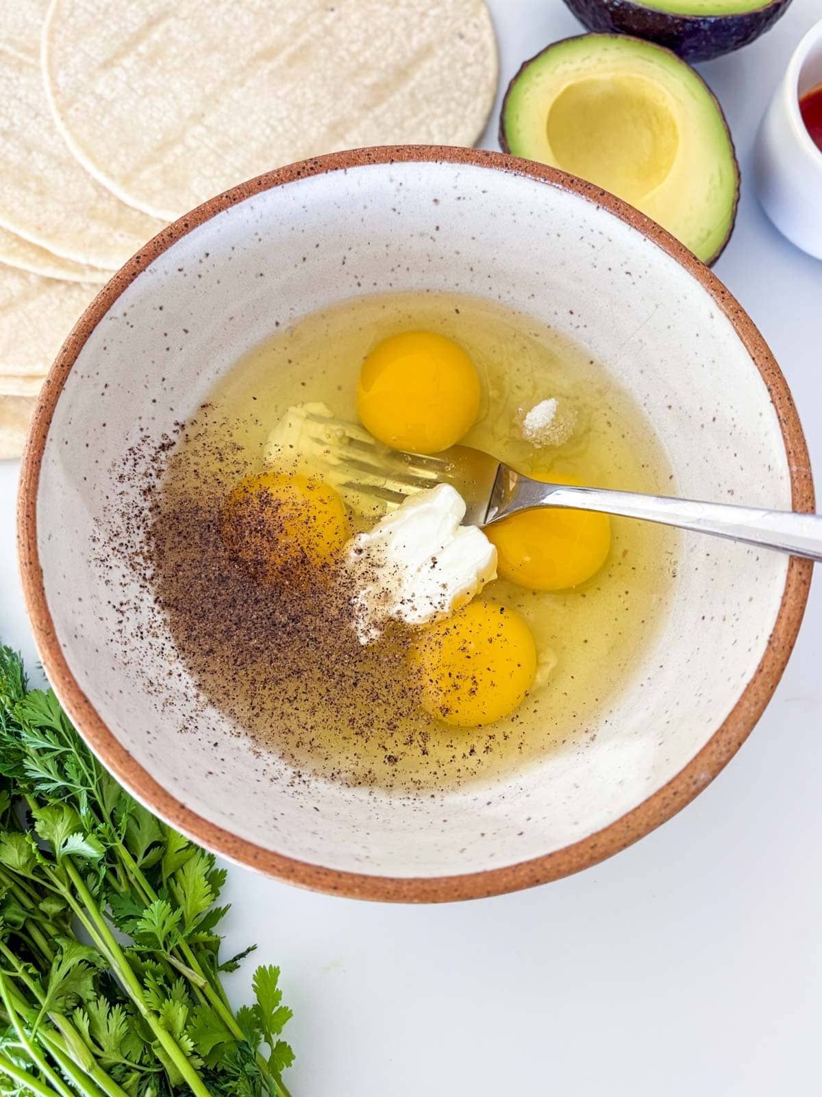 ceramic bowl with eggs, sour cream, salt, and pepper, with a fork.