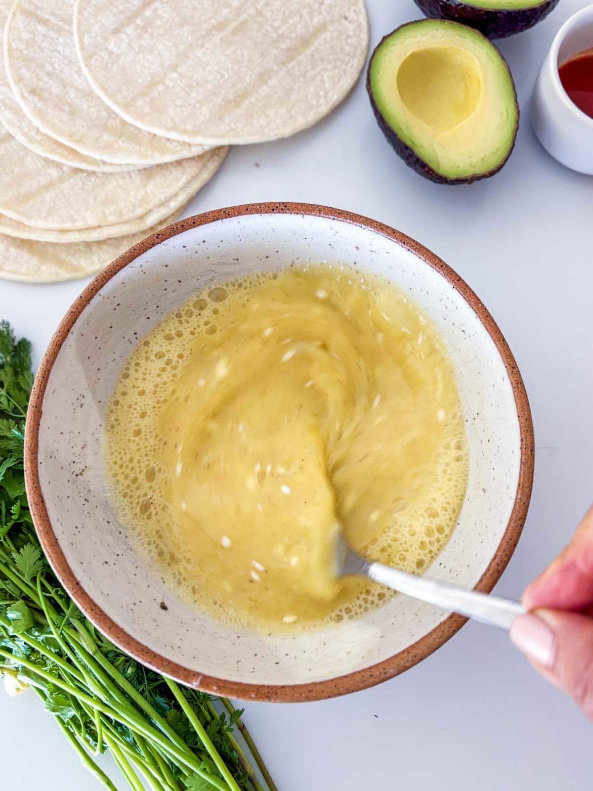 fork whisking eggs in a ceramic bowl to make breakfast tacos.
