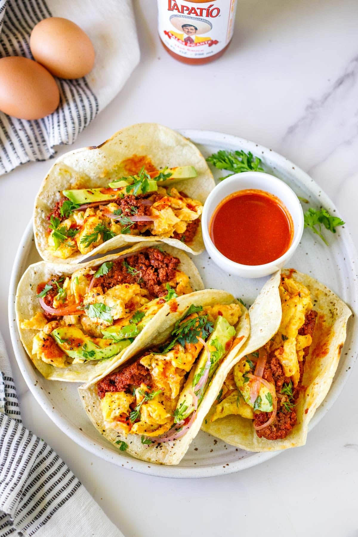 four egg and chorizo breakfast tacos on a plate with a bowl of hot sauce.
