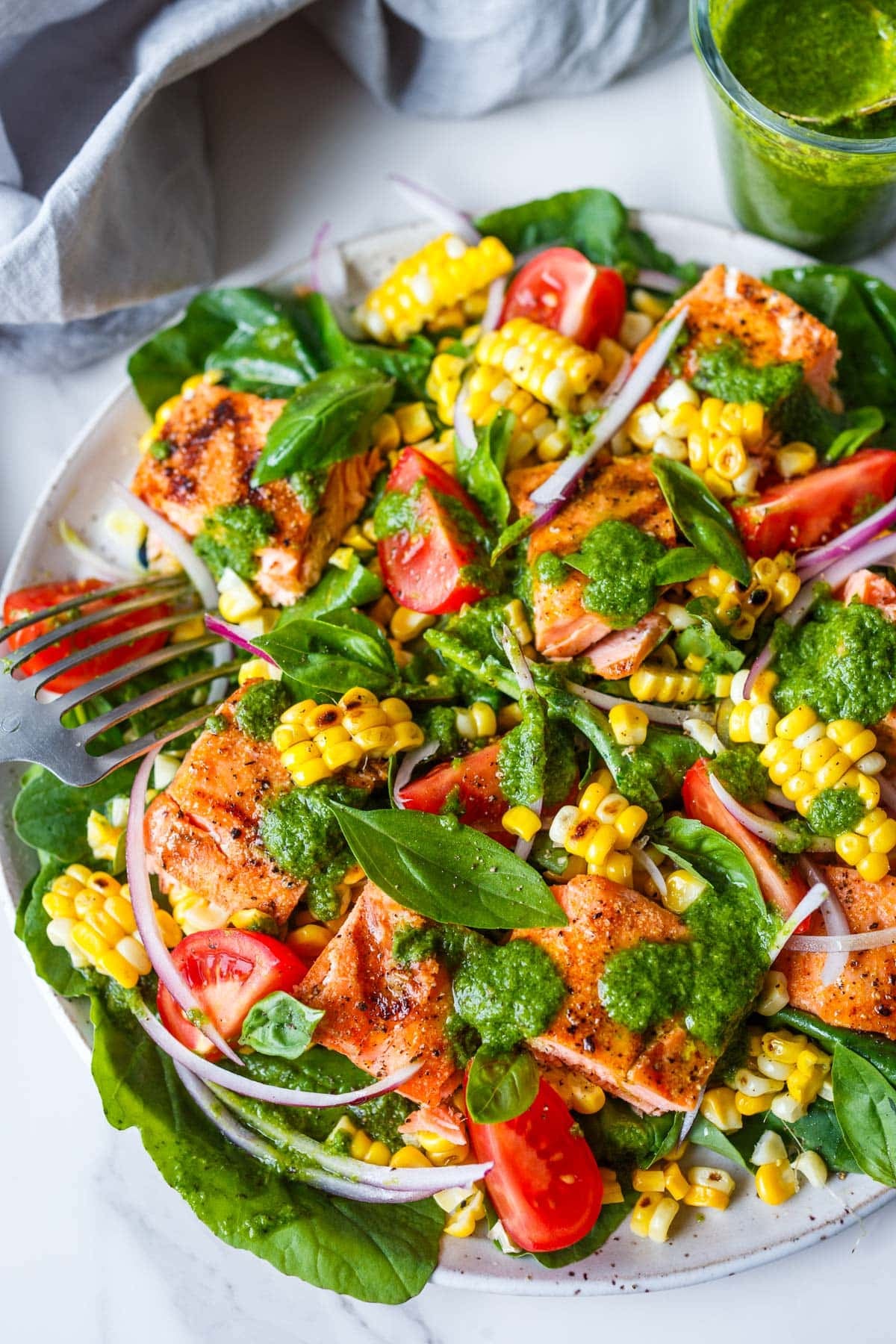 summer corn, tomato, and salmon salad with red onion and basil with basil vinaigrette drizzled over top.