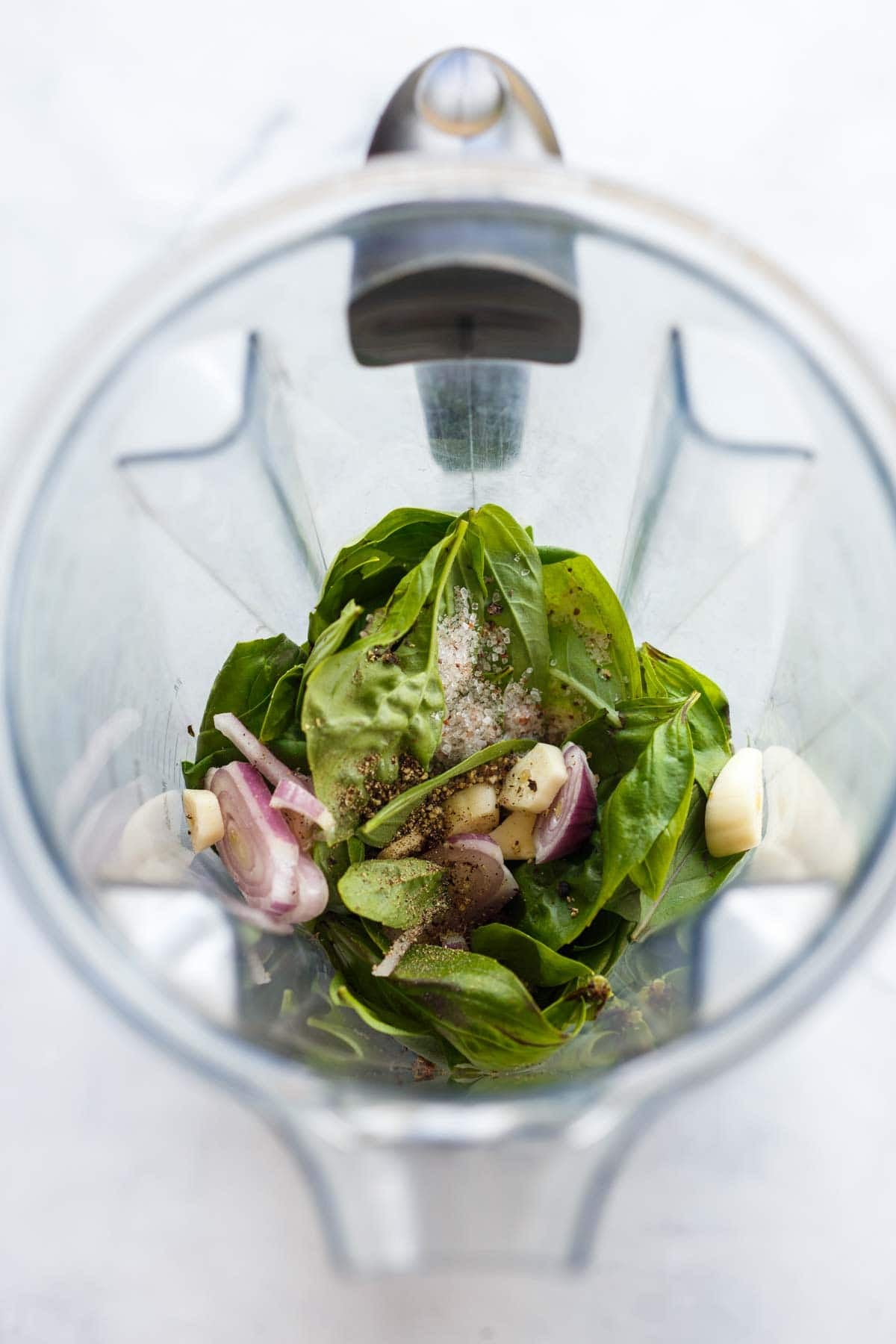 blender with basil vinaigrette ingredients - basil, garlic cloves, shallots, salt, and pepper.