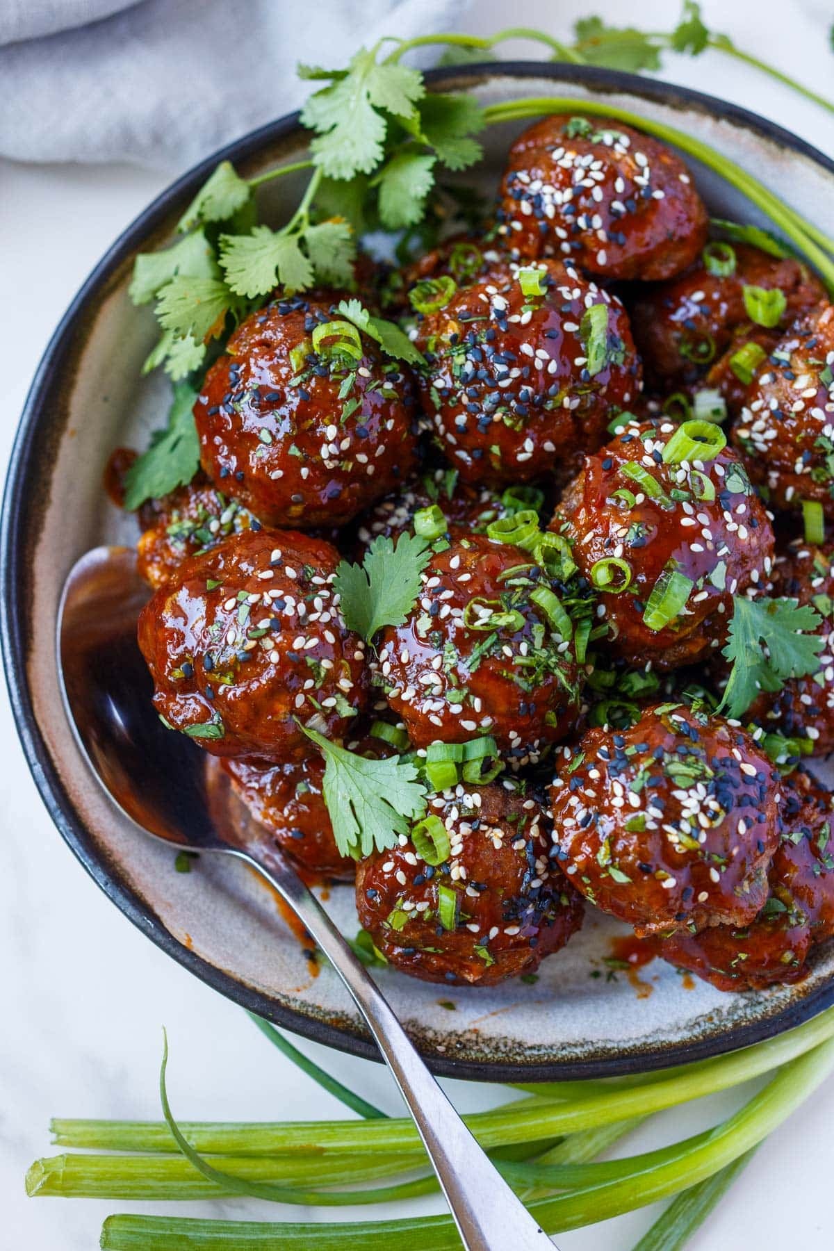 bowl of Korean meatballs topped with herbs, green onions, and sesame seeds, with a spoon.