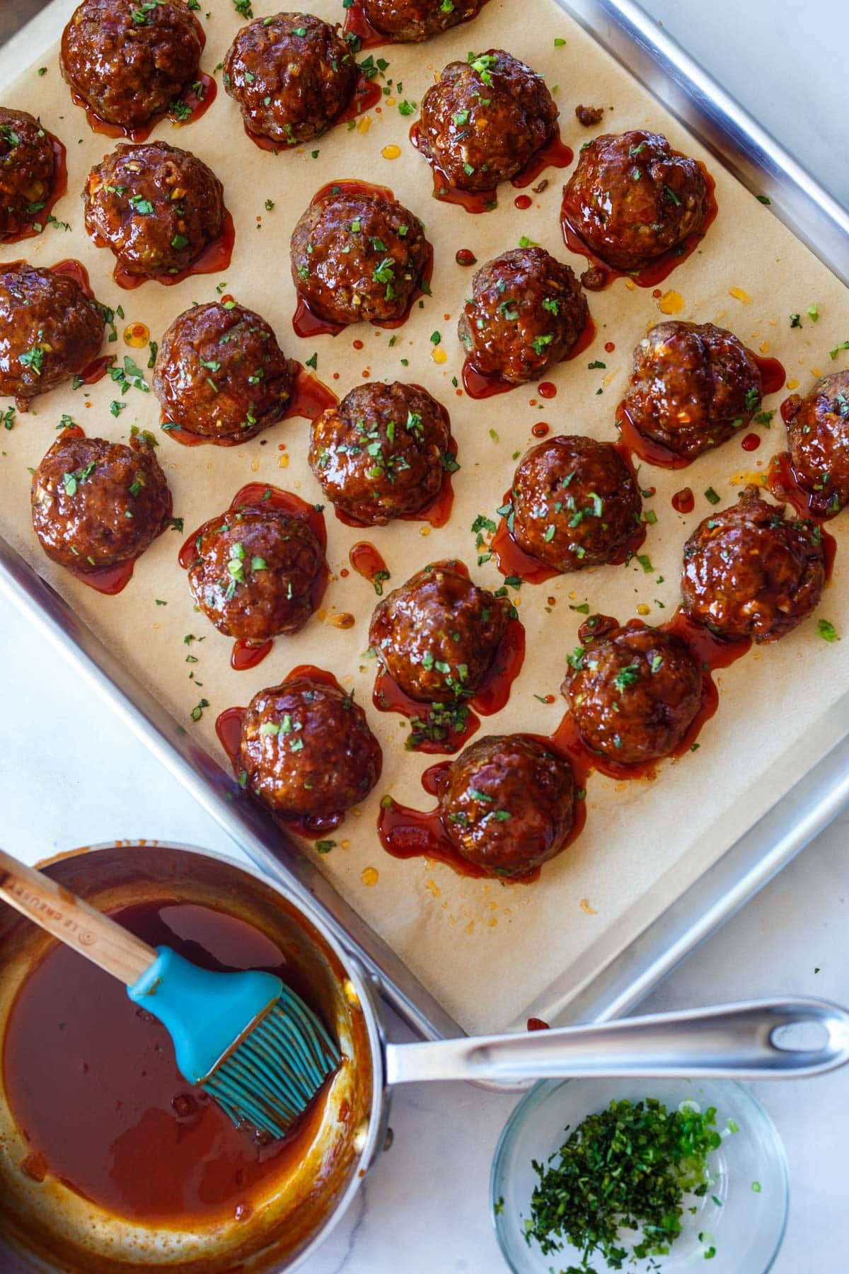 cooked Korean meatballs on a parchment-lined baking sheet and covered in the glaze and garnished with herbs.