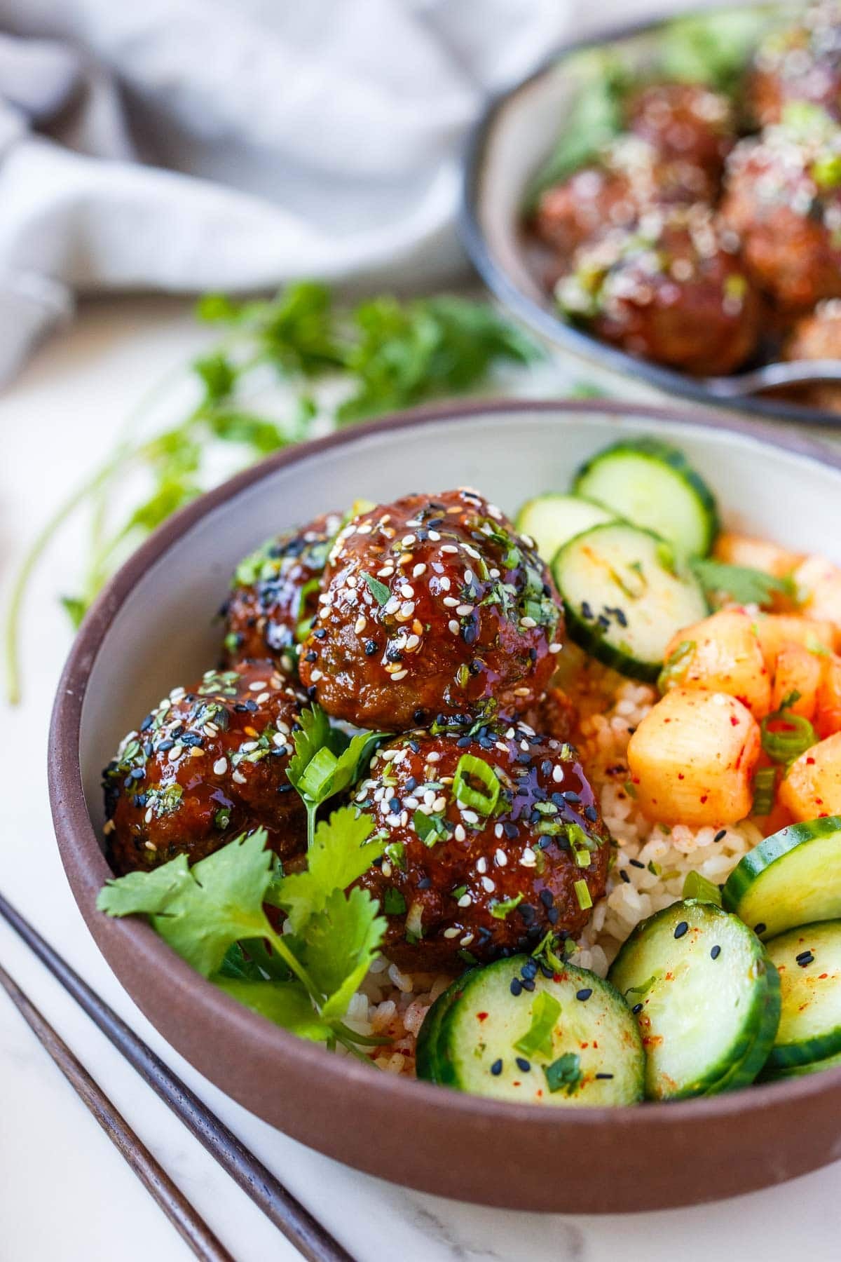 bowl of Korean meatballs, steamed rice, cucumbers, and pickled daikon.