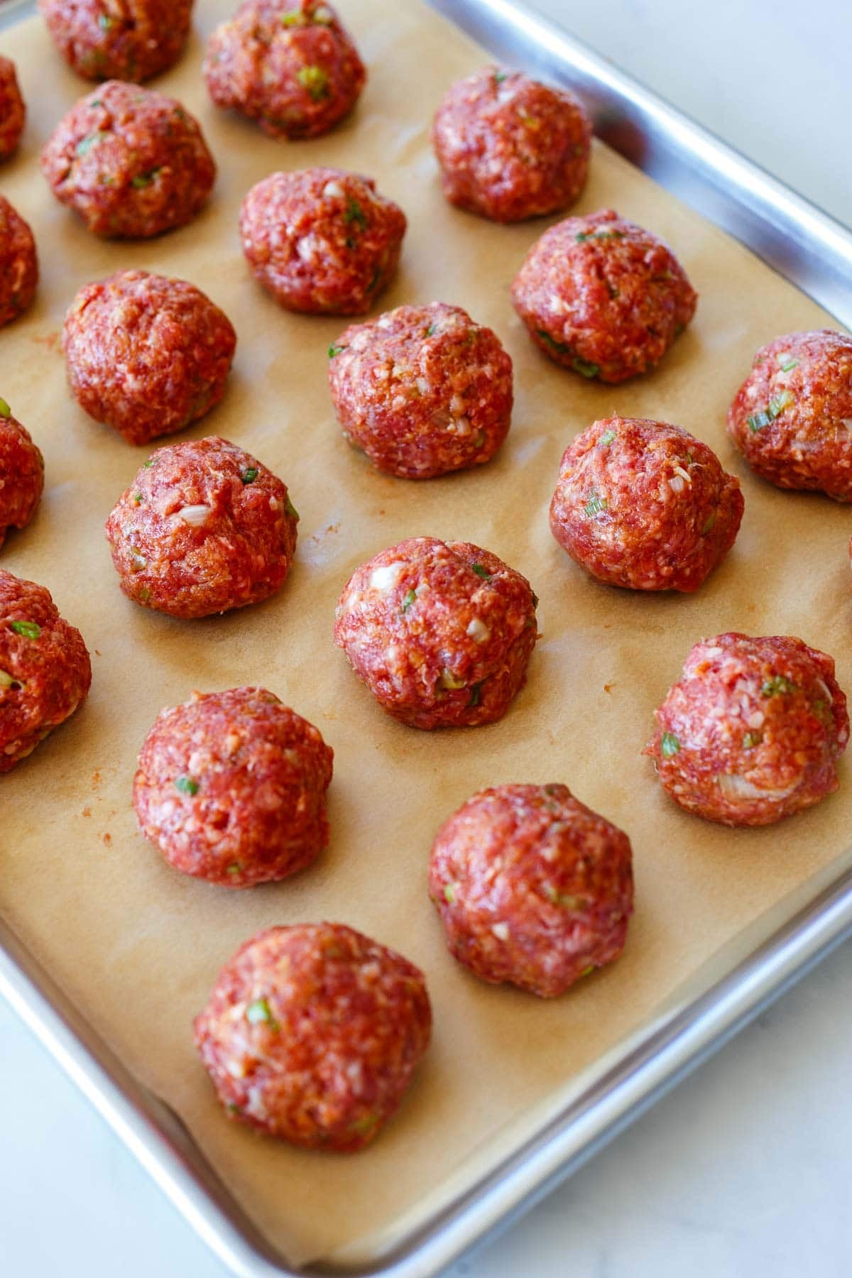 Korean meatballs formed and spread out evenly on a parchment-lined baking sheet.