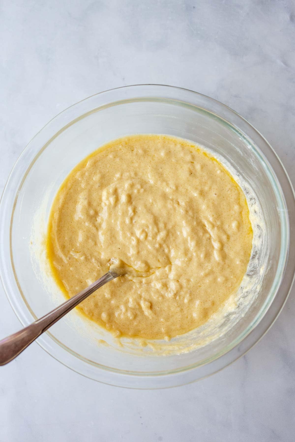 batter for strawberry cobbler in a glass mixing bowl with a silver utensil.