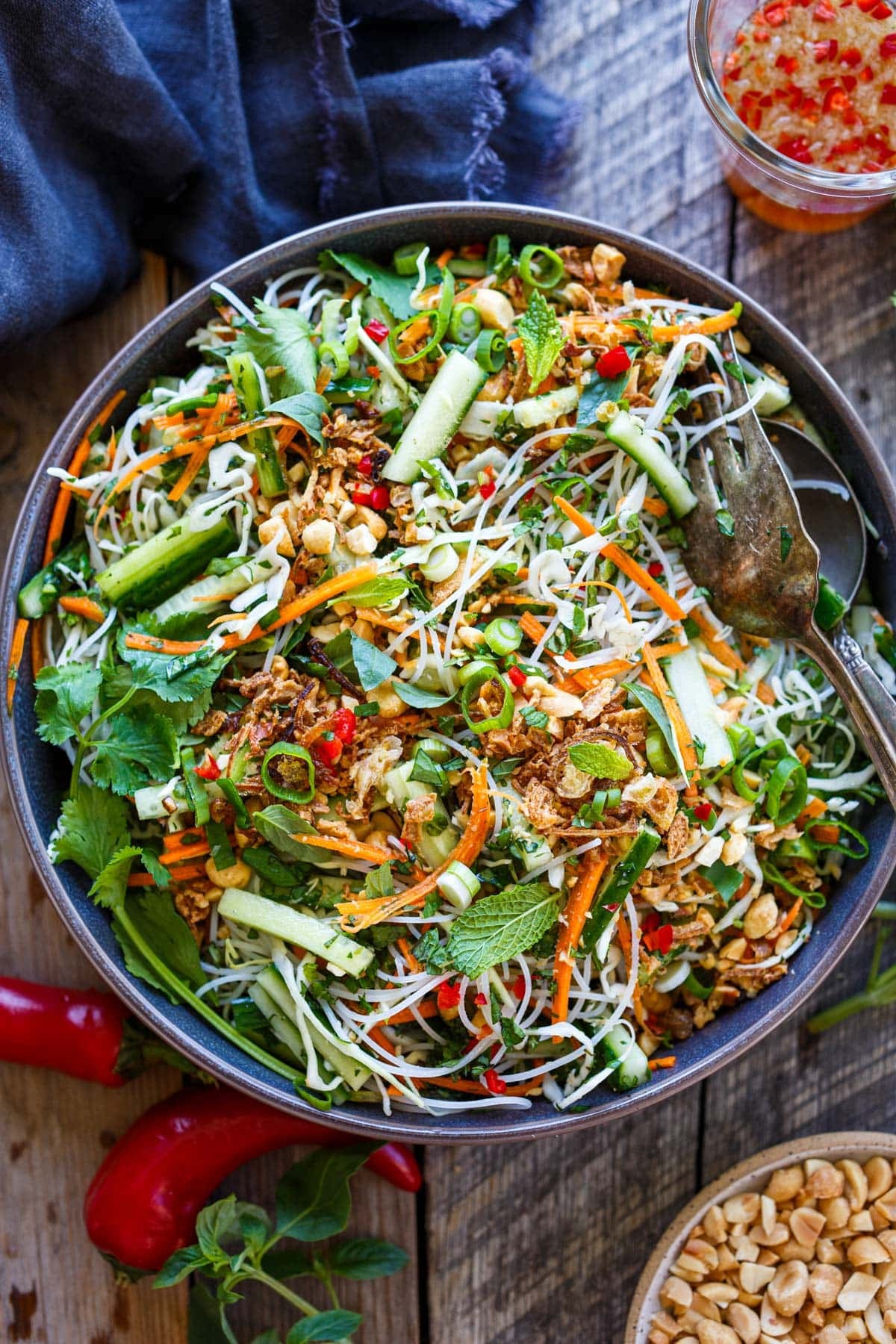 vermicelli salad with fresh veggies, like cucumber and carrot, herbs, peanuts, and crispy shallots in a bowl with silver serving utensils.
