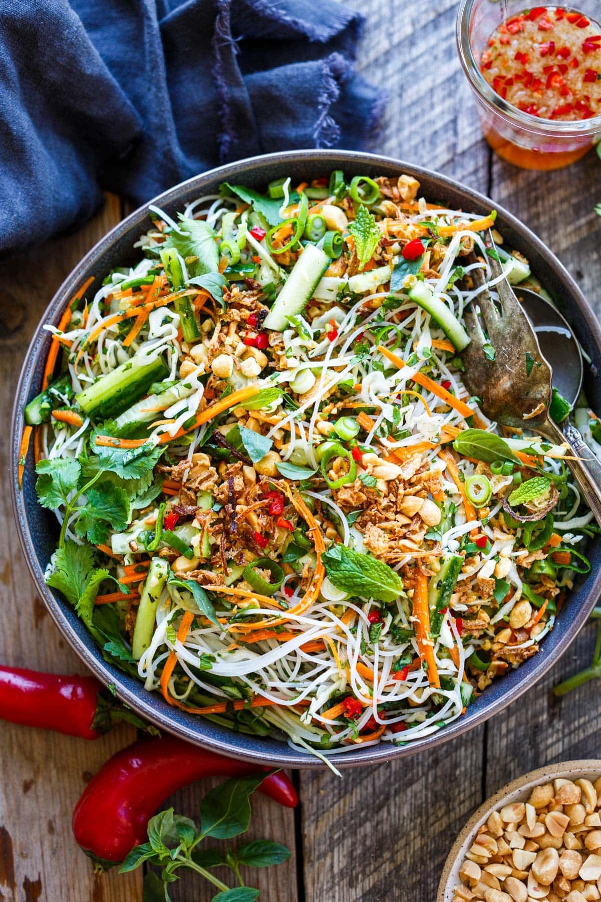 salad bowl and utensils with Vietnamese vermicelli salad with cucumber, carrot, peanuts, crispy shallots, herbs, and red chilies.