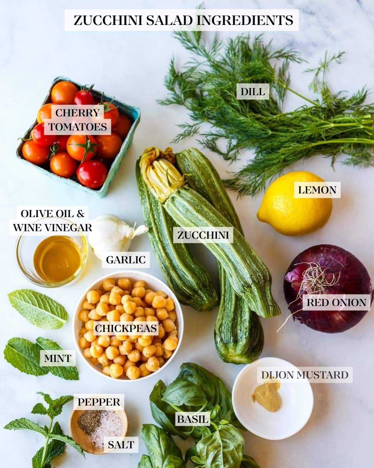 ingredients for zucchini salad - cherry tomatoes, dill, young zucchini, lemon, red onion, garlic bulb, olive oil in small glass bowl, small white bowl of chickpeas, fresh mint, pinch bowl with salt and pepper, fresh basil, small white bowl with Dijon mustard.