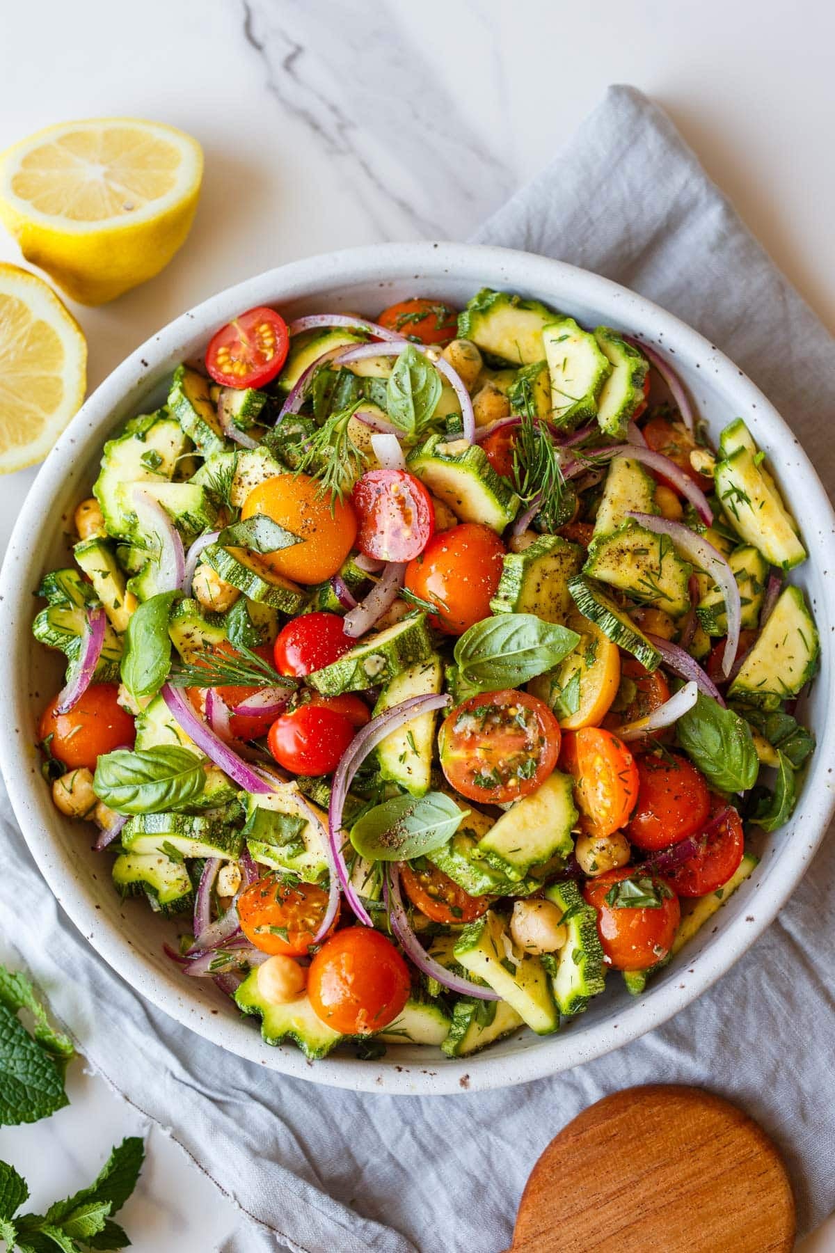 zucchini salad with cherry tomatoes, red onion, herbs, and chickpeas in a white bowl.
