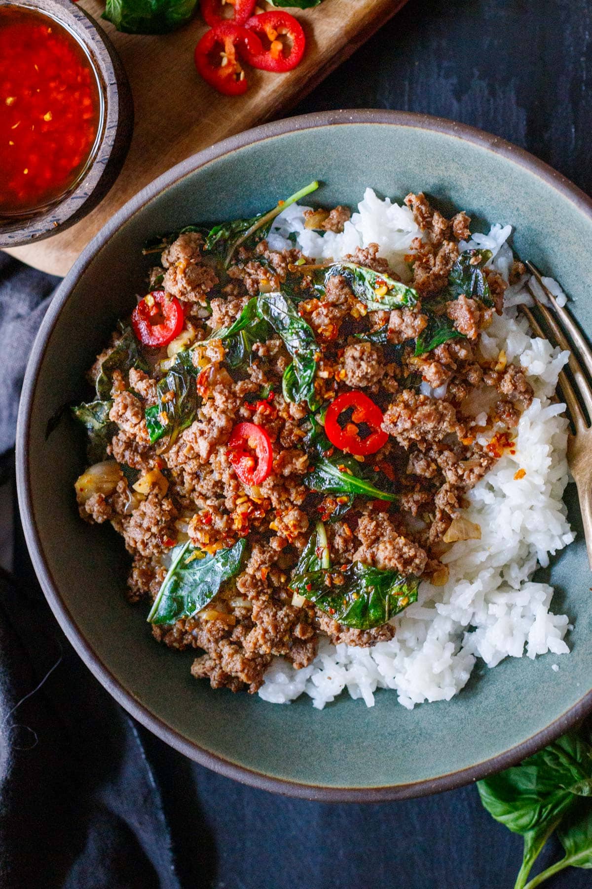 bowl of basil beef with steamed jasmine rice with red chilies and chili crisp and a fork. 