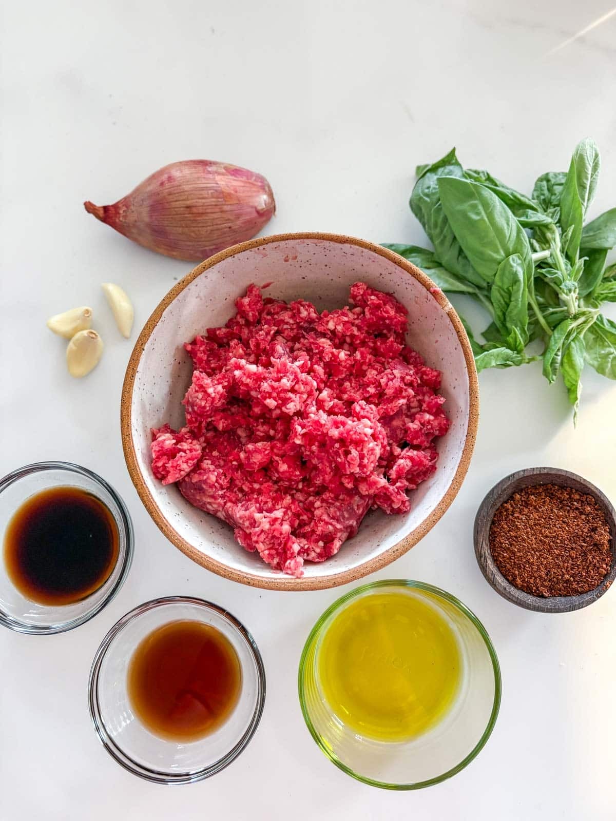 ingredients for basil beef - shallot, fresh basil, garlic cloves, ground beef, chili flakes, olive oil, fish sauce, and soy sauce, arranged neatly in bowls.  