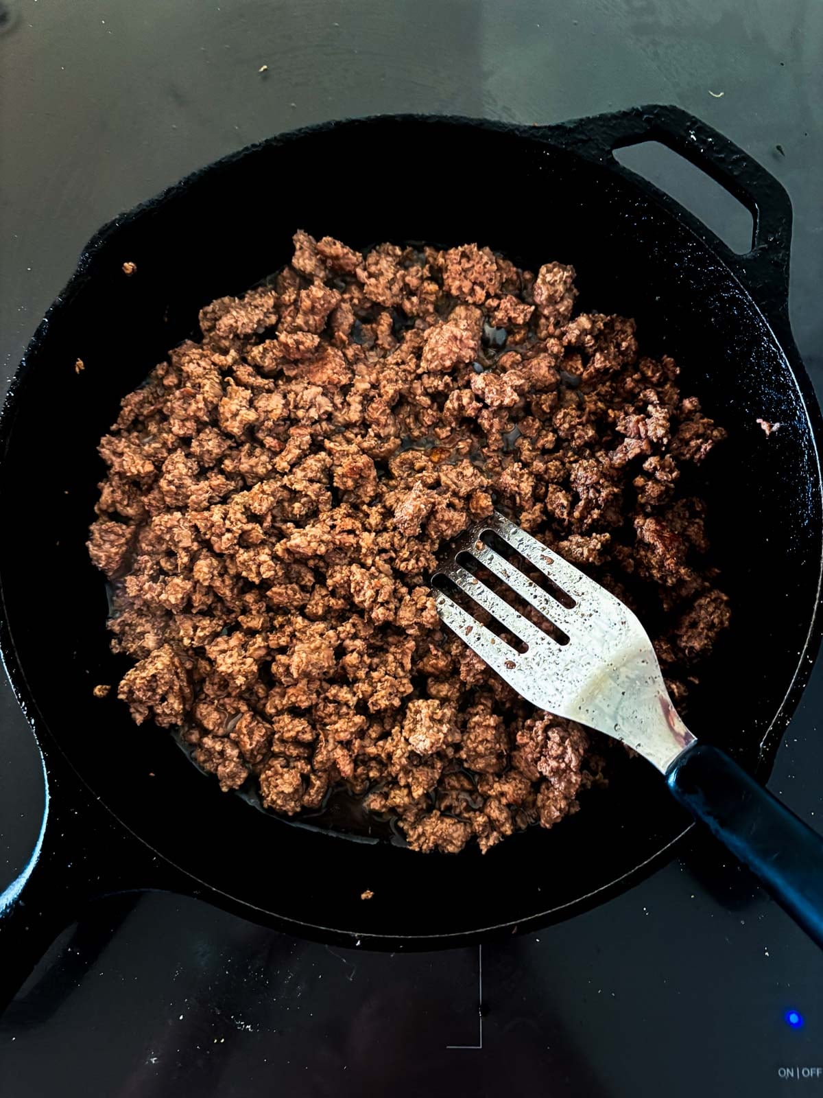 ground beef browning in a cast iron skillet with a spatula to make basil beef.