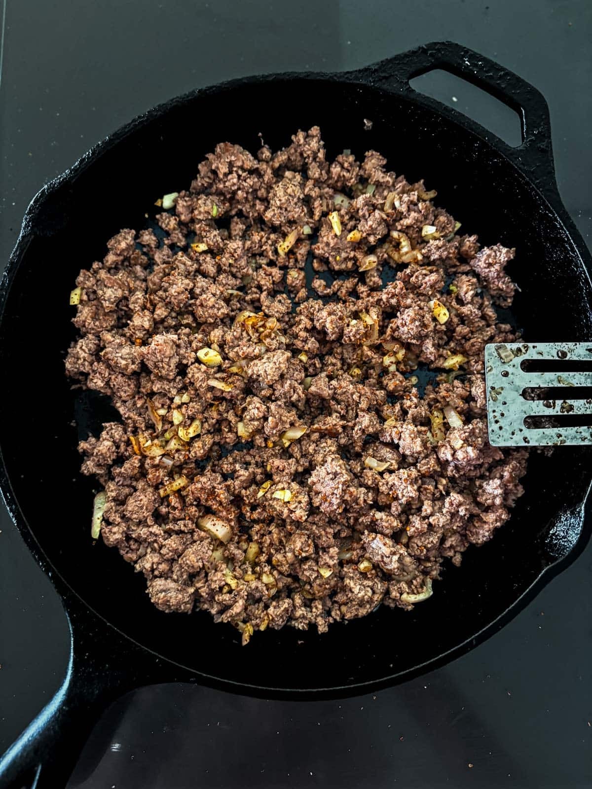 combining ground beef with sautéed aromatics in a cast iron skillet to make basil beef.