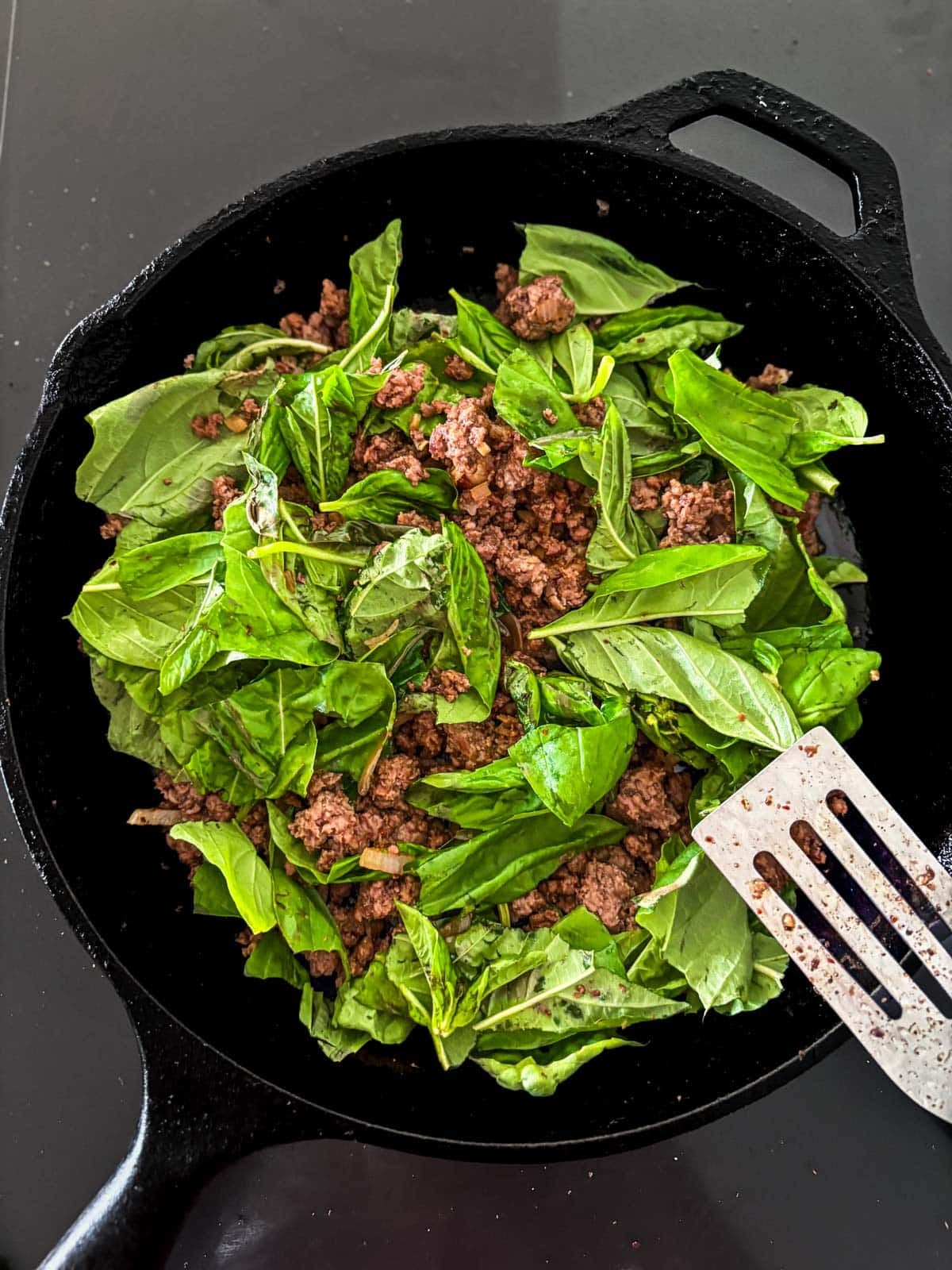 fresh basil and ground meat in a cast iron skillet to make basil beef.