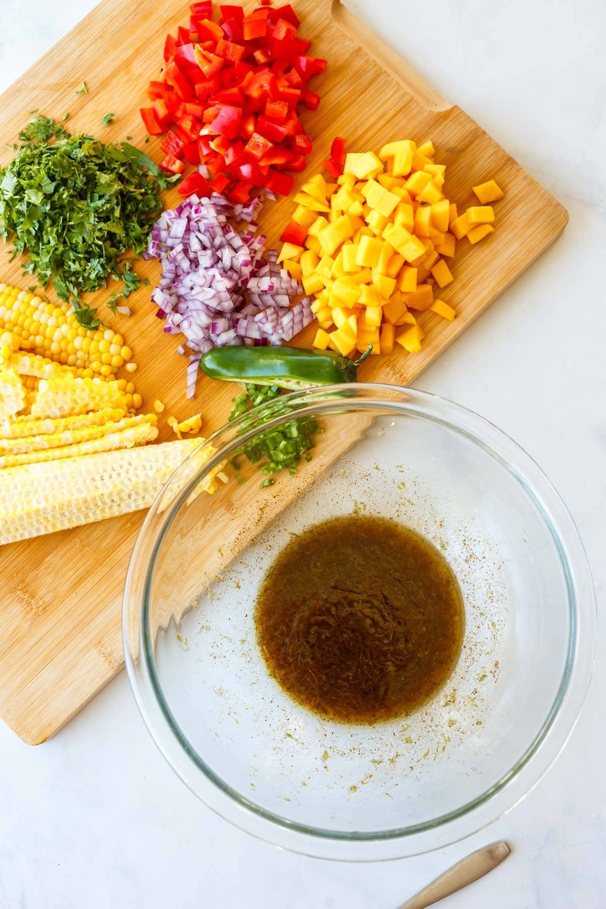large glass bowl with chili lime dressing next to wood cutting board with chopped veggies for black bean salad.