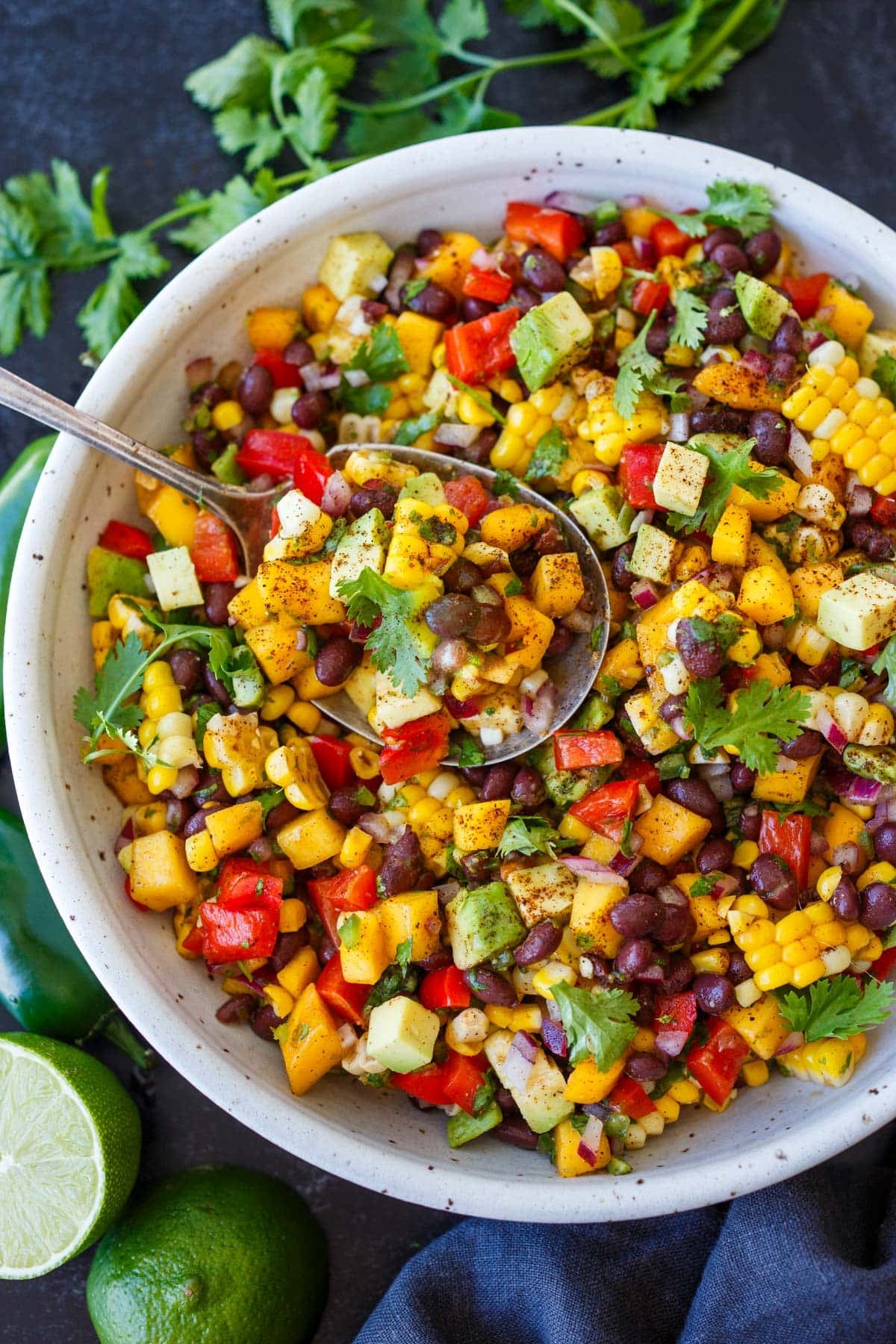black bean salad with bell pepper, avocado, red onion, cilantro, mango, and corn in a ceramic bowl with a spoon lifting a spoonful up.