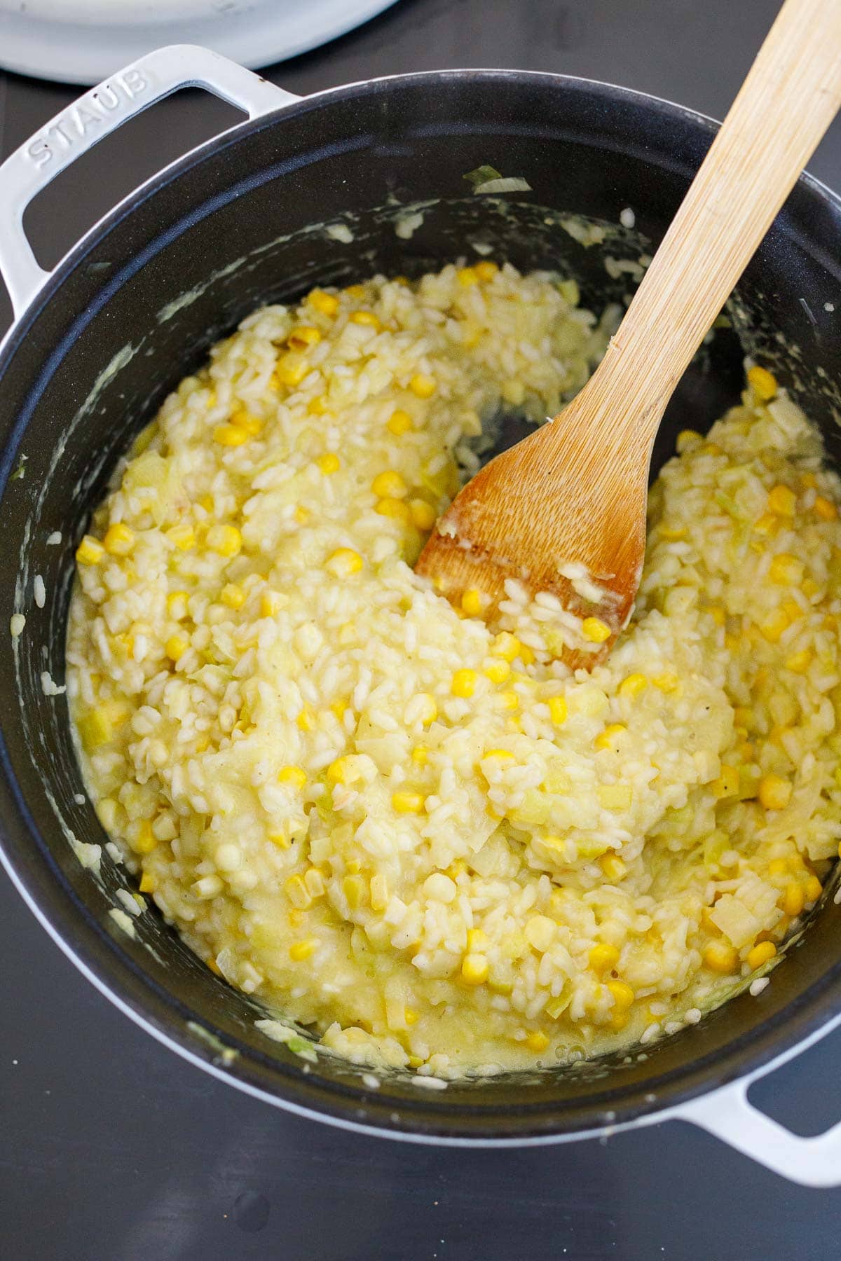 wood spatula stirring corn risotto in a Dutch oven.