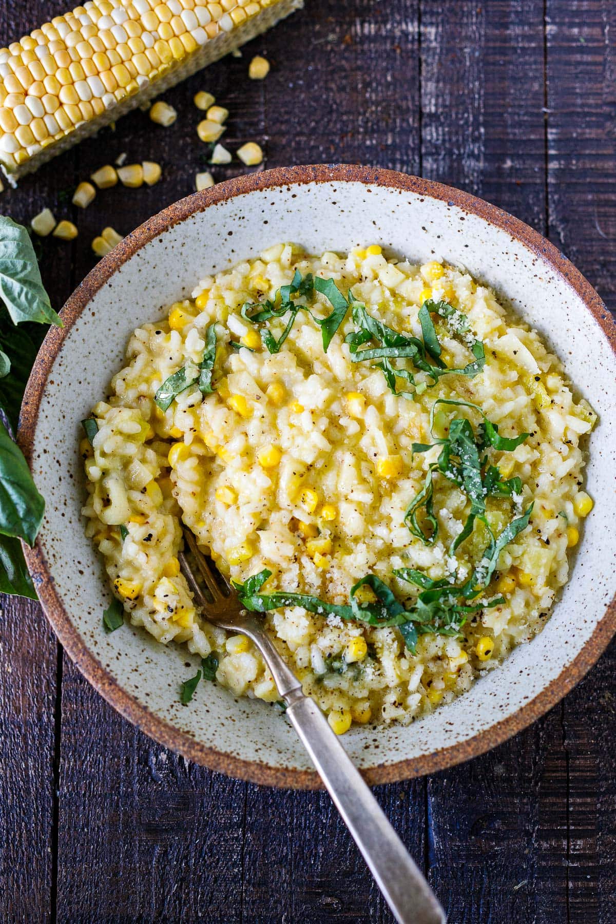 ceramic bowl with sweet corn risotto topped with fresh basil ribbons with a fork.