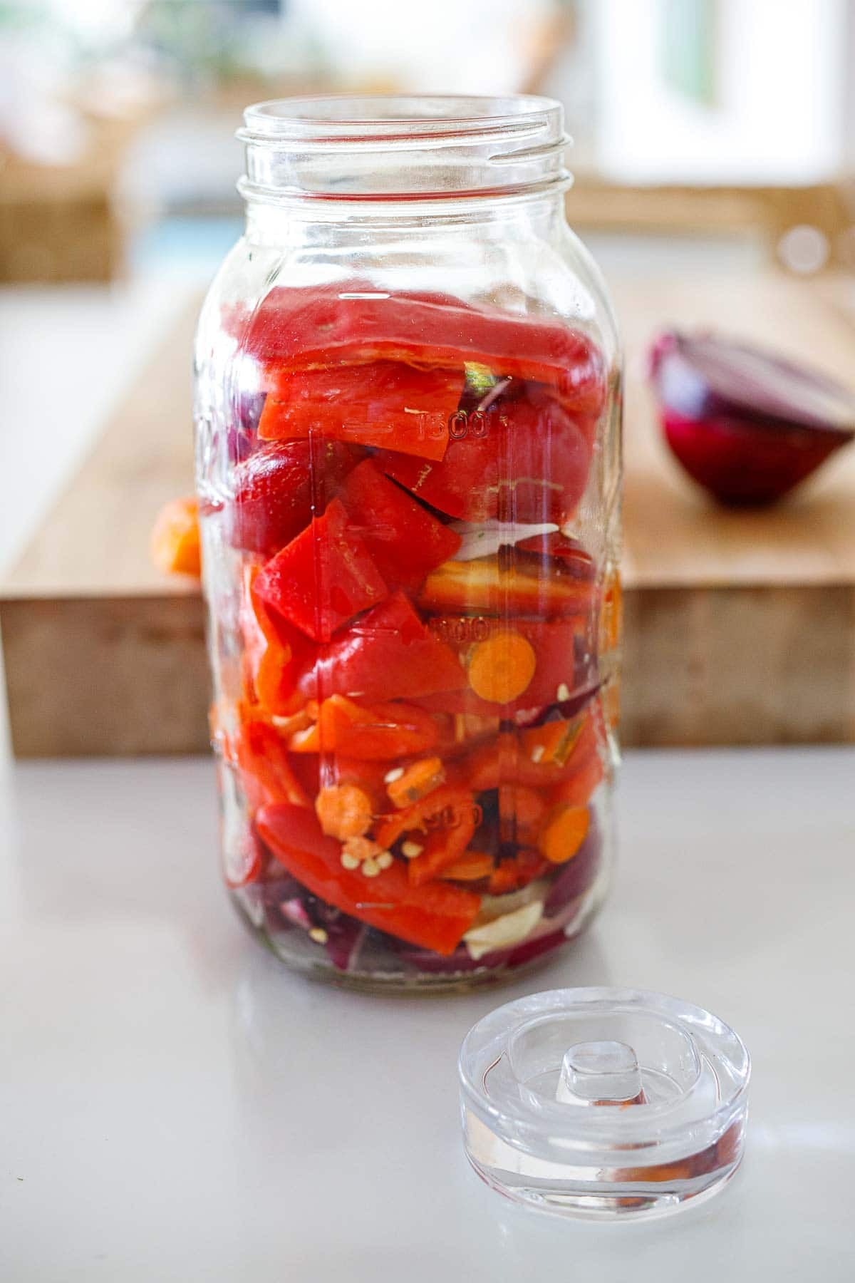 Red chilies layered in a mason jar with onions, carrots and garlic, to be fermented. 