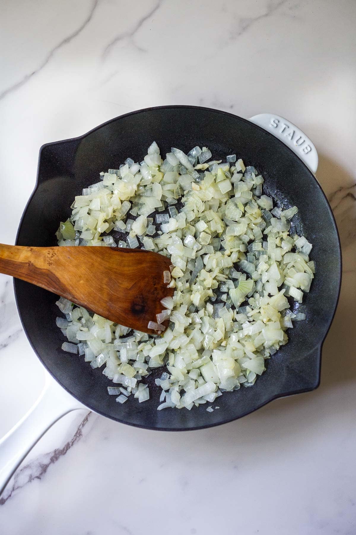 Making the greek orzo: diced onions sautéing in a skillet with a wood spatula.
